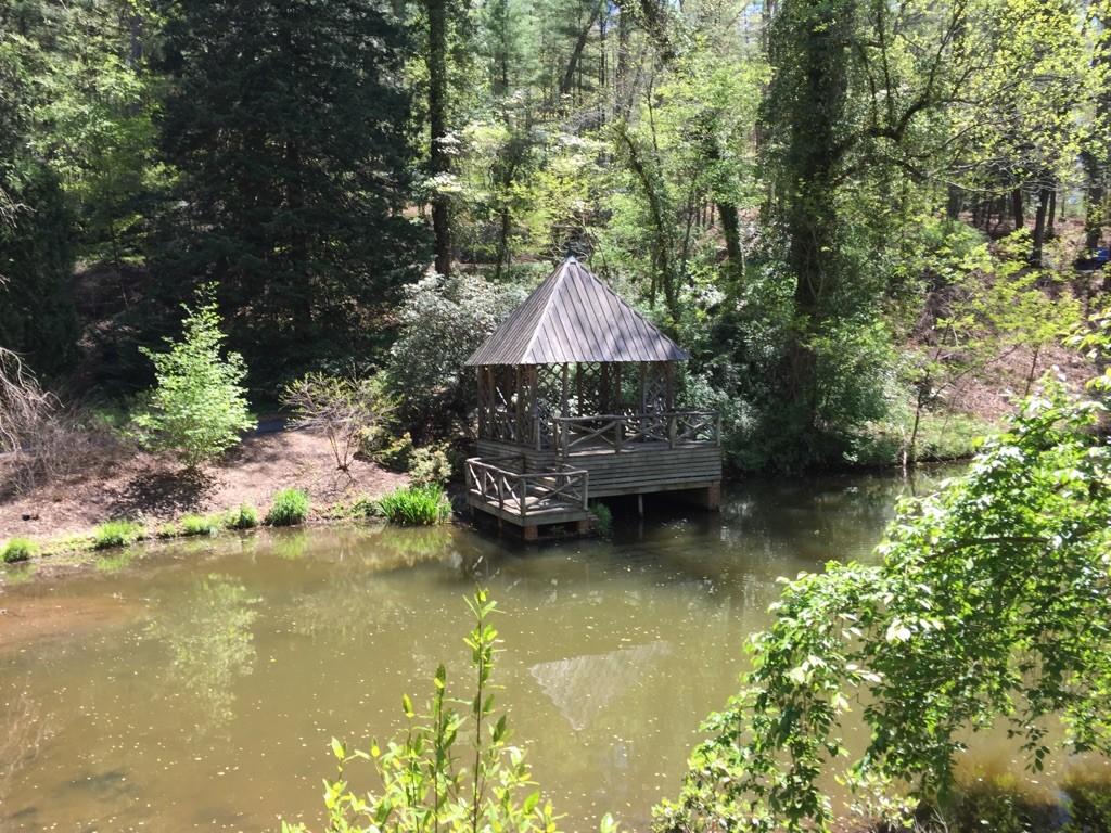 Wooden gazebo on a dock over a calm pond, surrounded by green trees.