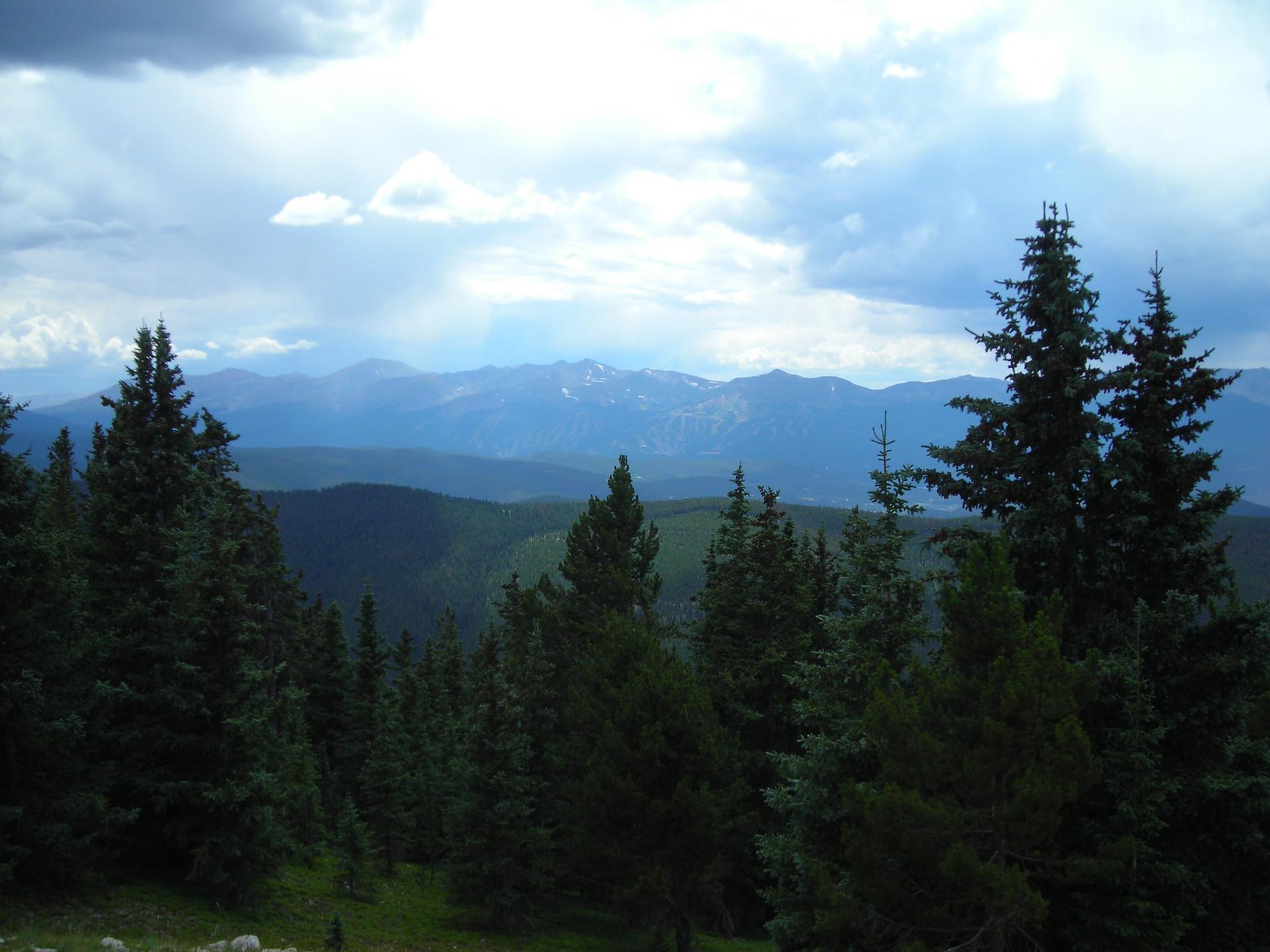 Evergreen forest and distant mountains under a dramatic, cloudy sky.