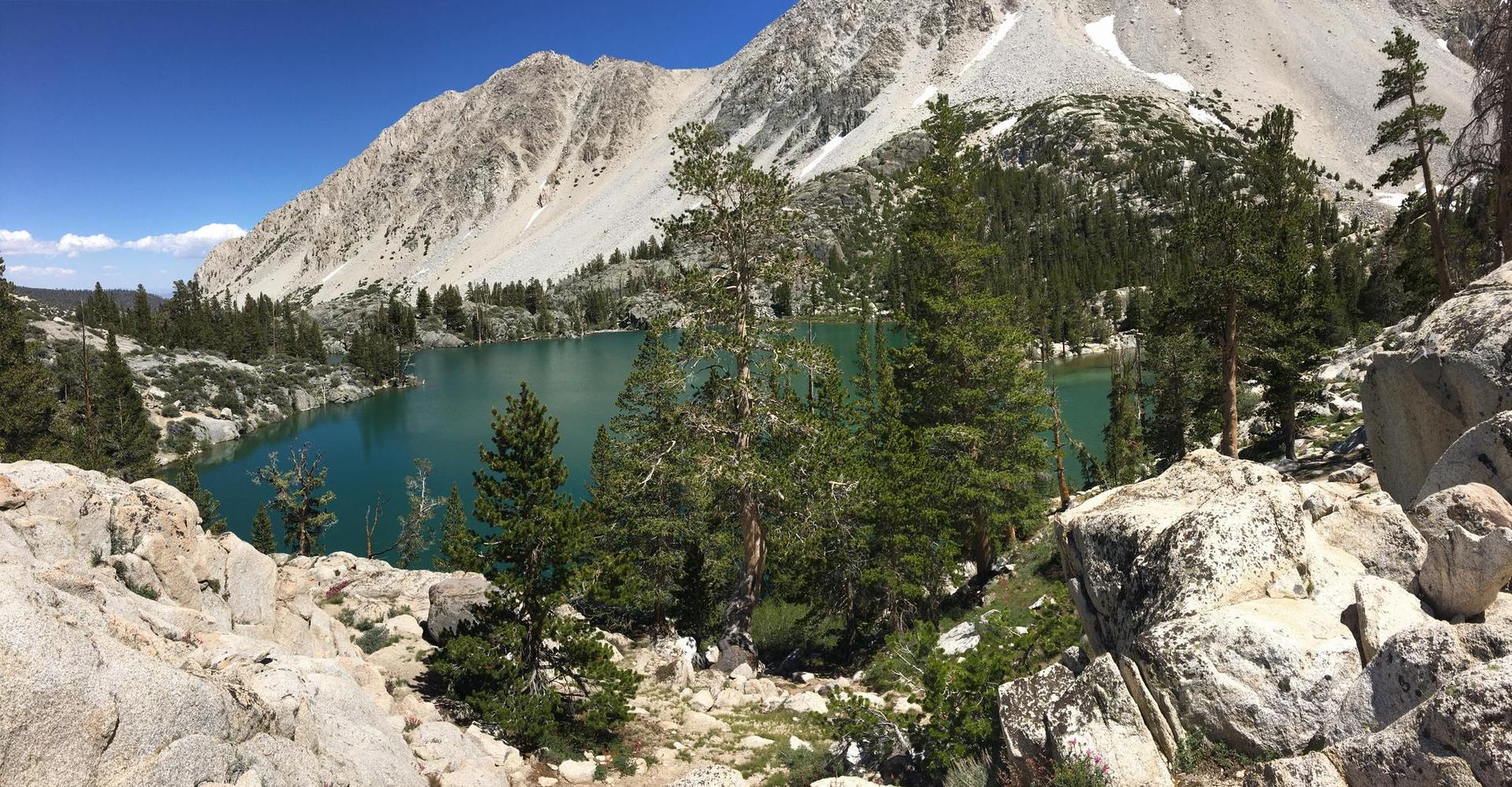 Turquoise mountain lake with rocky foreground and distant peaks under blue sky.
