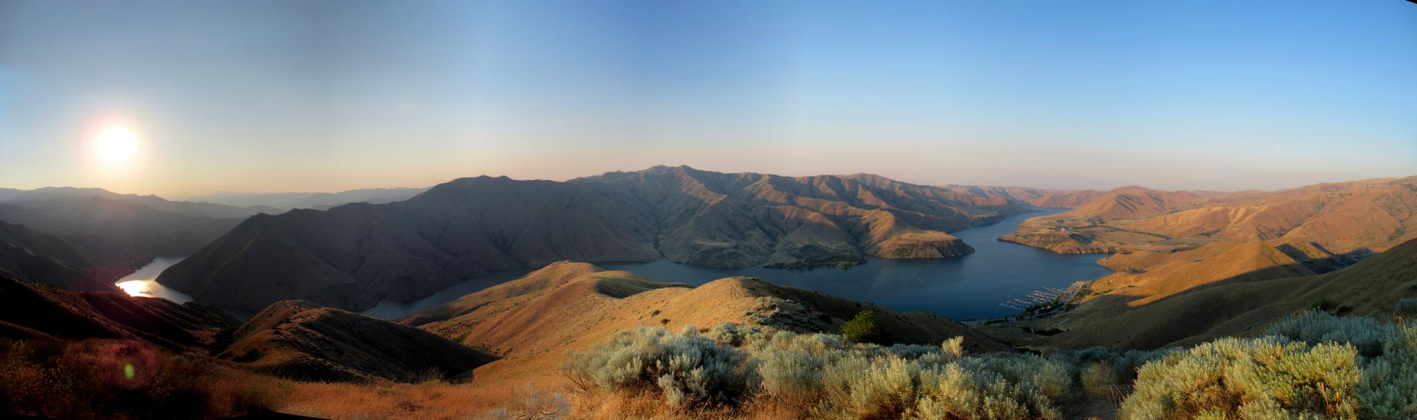 Panoramic view of arid mountains and a winding lake at sunset.