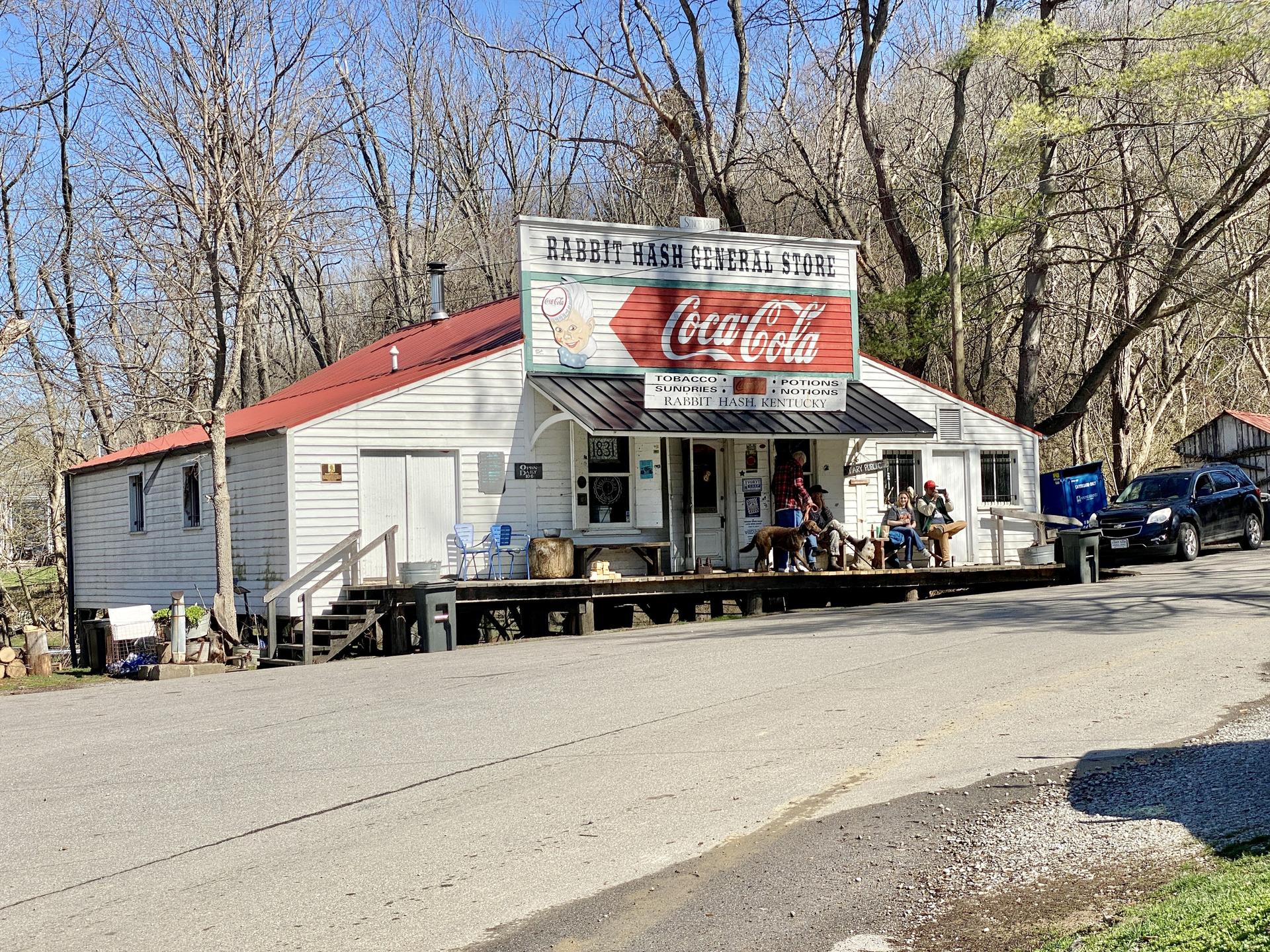 An old general store with a red roof and people on the porch.