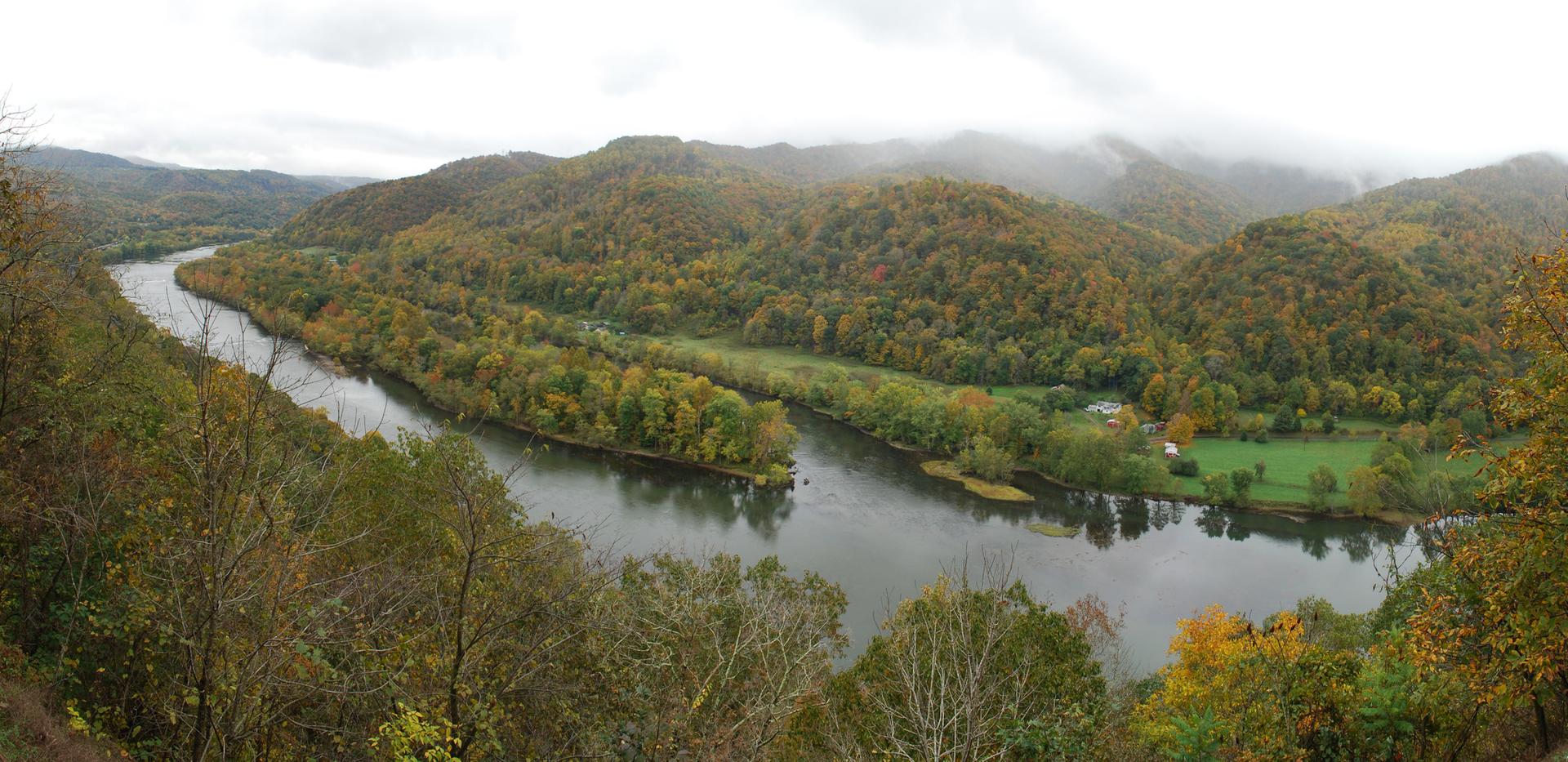 Winding river through autumn-colored forested hills under an overcast sky.