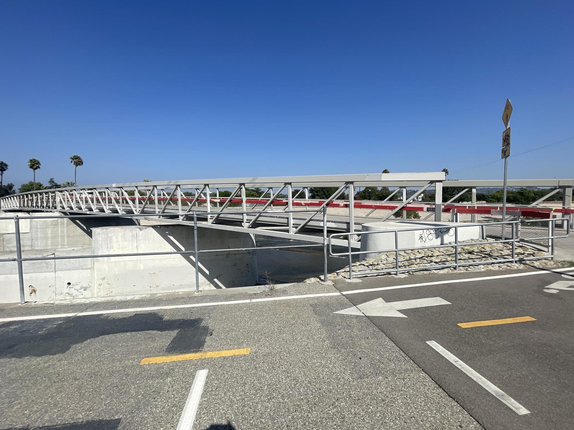 Modern grey truss bridge over a concrete channel under a clear blue sky.