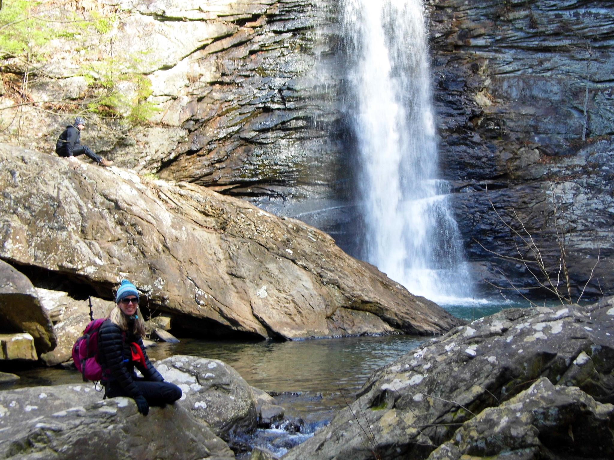 Two people near a powerful waterfall cascading into a rocky pool.