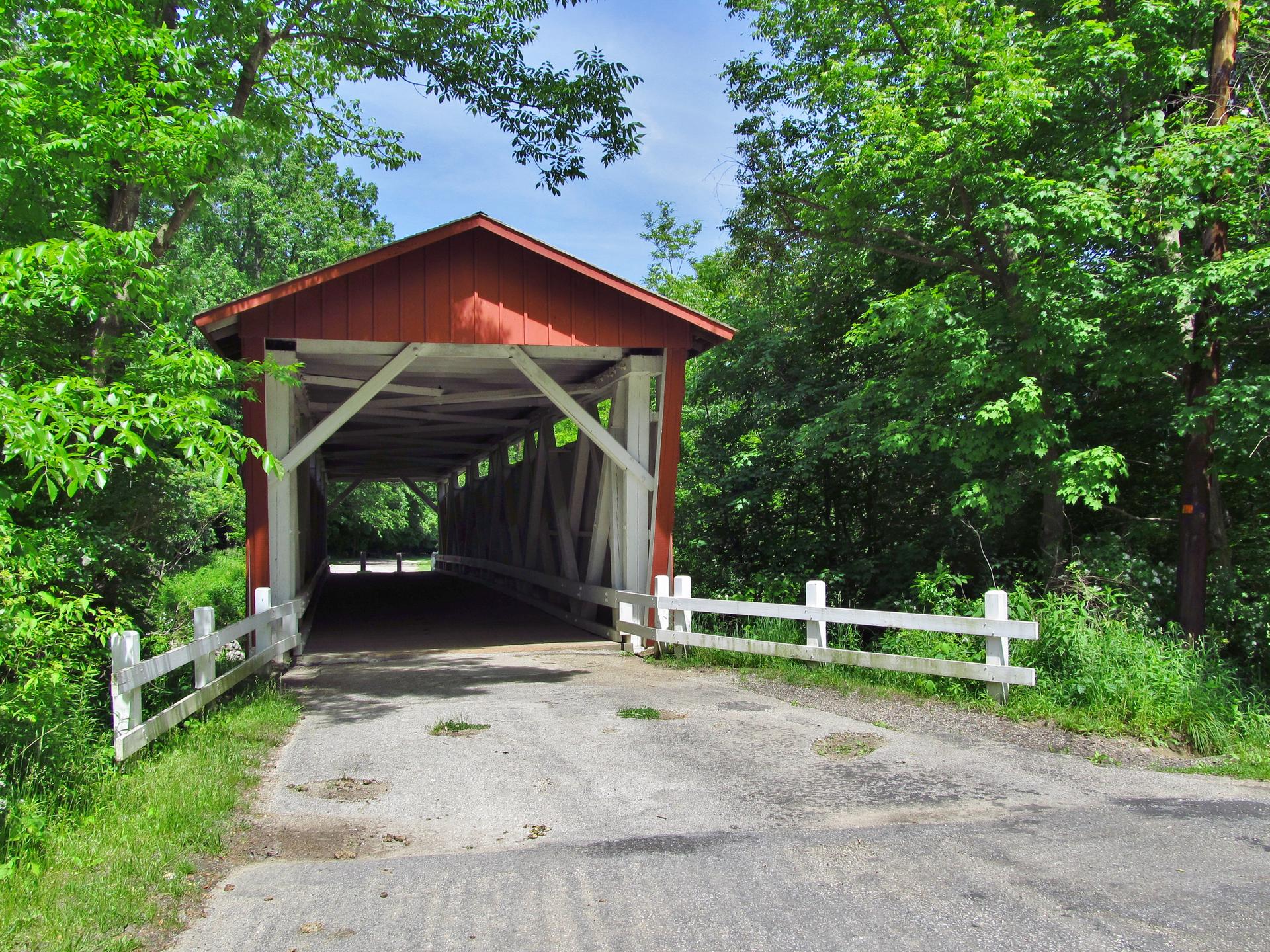 A red covered bridge surrounded by lush green trees on a sunny day.