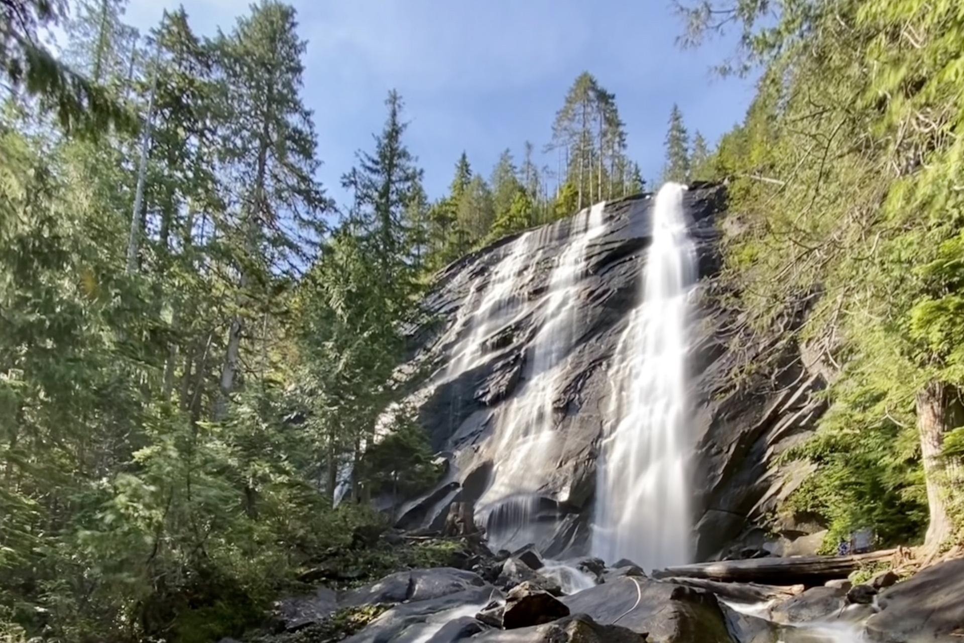 Majestic multi-tiered waterfall cascading down a rocky cliff in a sunlit forest.
