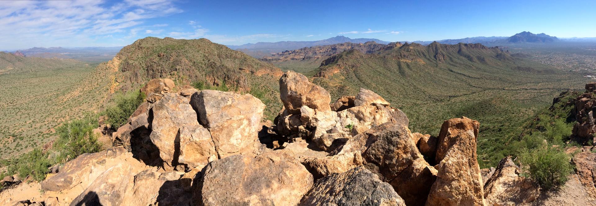 Panoramic view from a rocky peak overlooking a sprawling green desert valley.