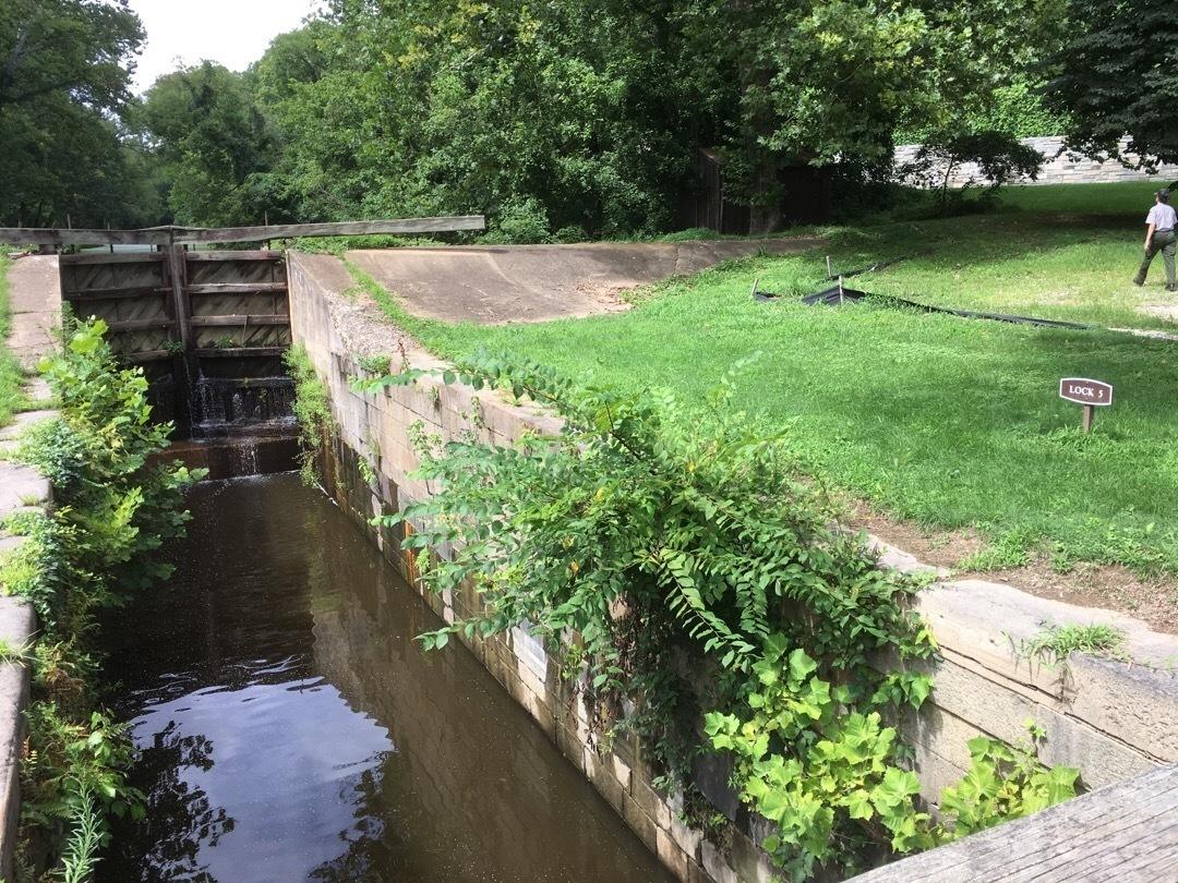 Water flowing through a canal lock with a person on the grassy bank.