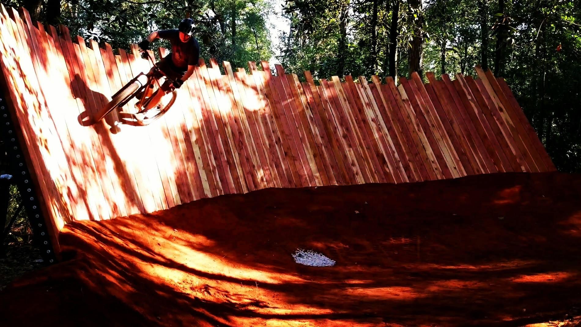 Mountain biker on a wooden wall ride in a sunny forest.