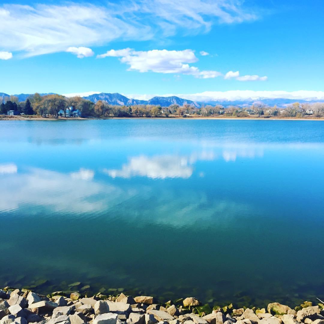 A calm blue lake with cloud reflections, rocky shore, and distant mountains.