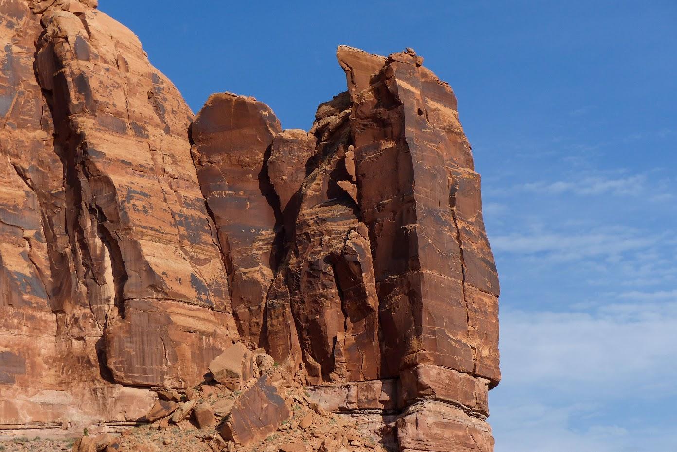 Close-up of towering red rock formations against a partly cloudy blue sky.