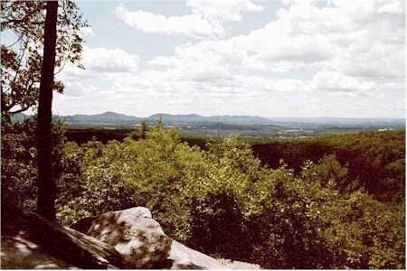 Expansive forest landscape with distant mountains under a cloudy sky, seen from a rocky outcrop. - Robert Frost Trail to Mount Orient