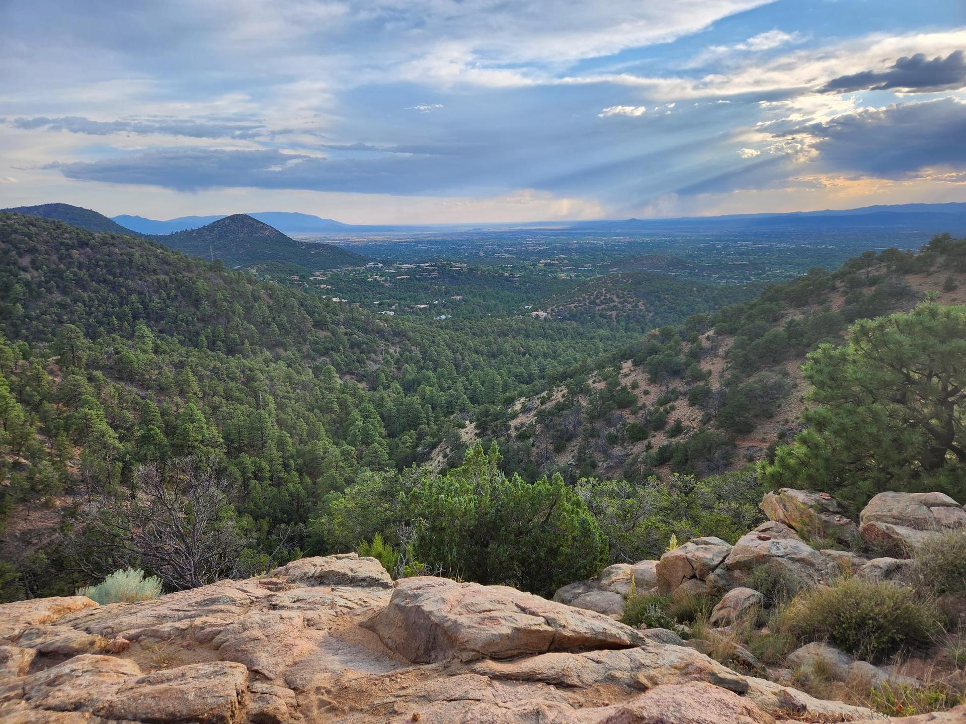 Expansive forested valley under a cloudy sky with sun rays.