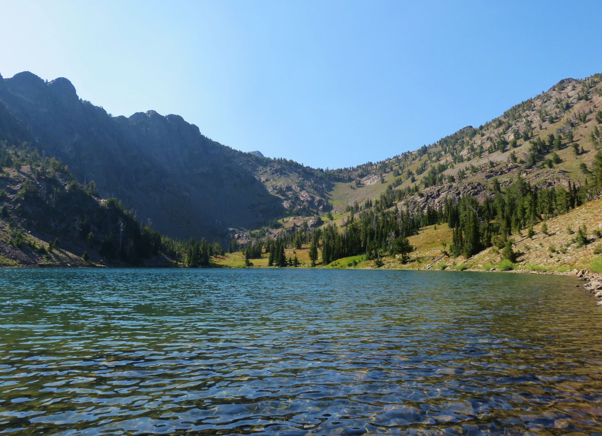 Clear mountain lake surrounded by steep, rocky, forested slopes under a blue sky. - Frog Lake Butte Twin Lakes Loop