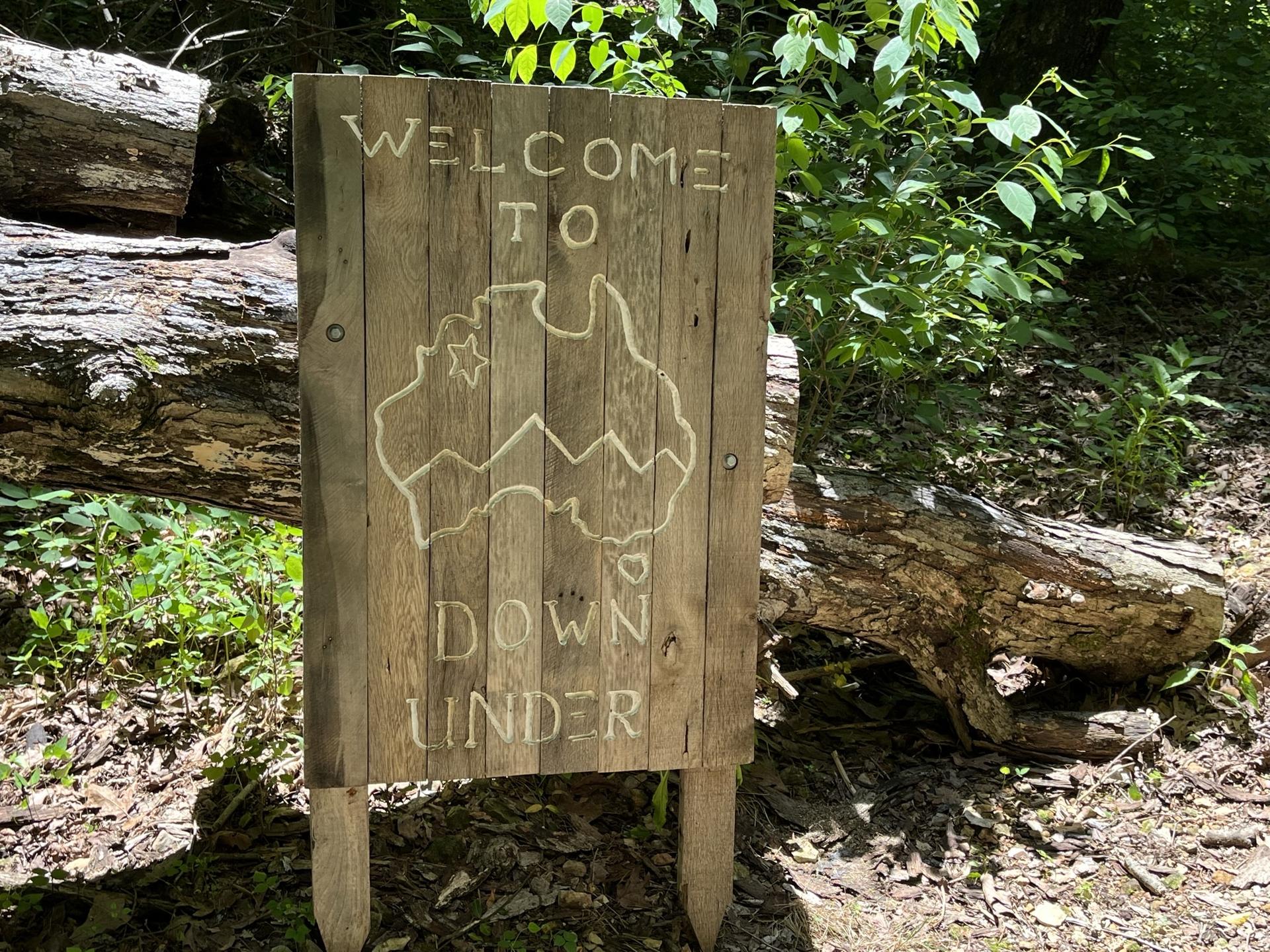 A wooden sign in a sunny forest, carved with "Welcome to Down Under".