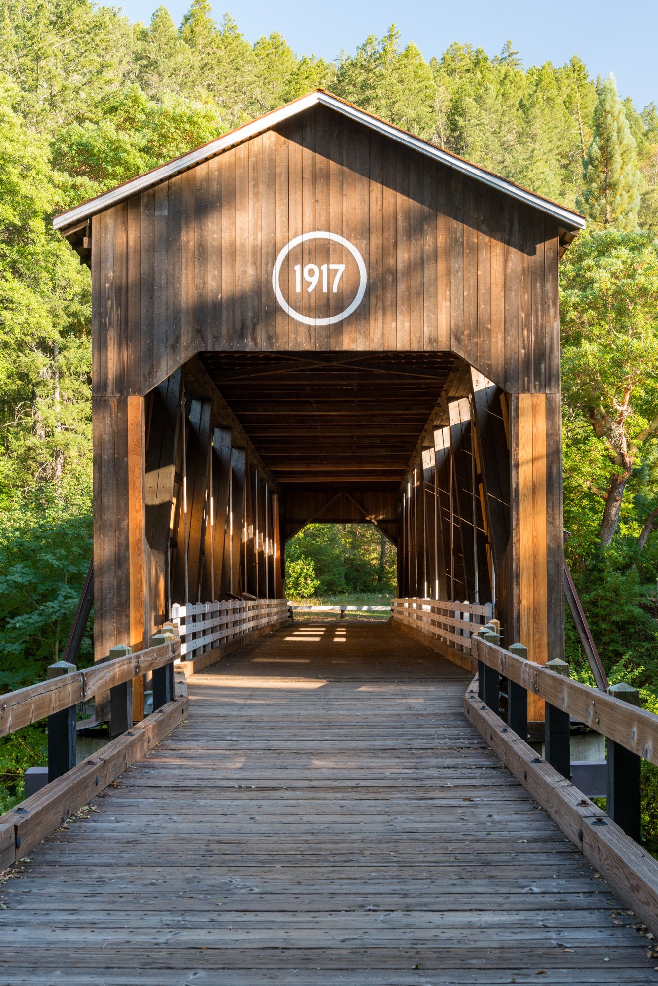 A long wooden covered bridge with a 1917 sign, surrounded by green trees. - Jacksonville - Applegate Lake loop