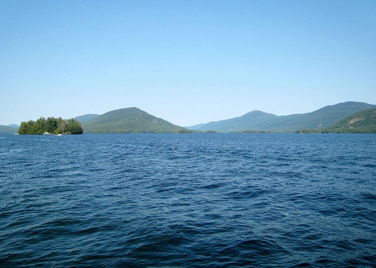 Wide blue lake with distant green mountains and a small forested island.