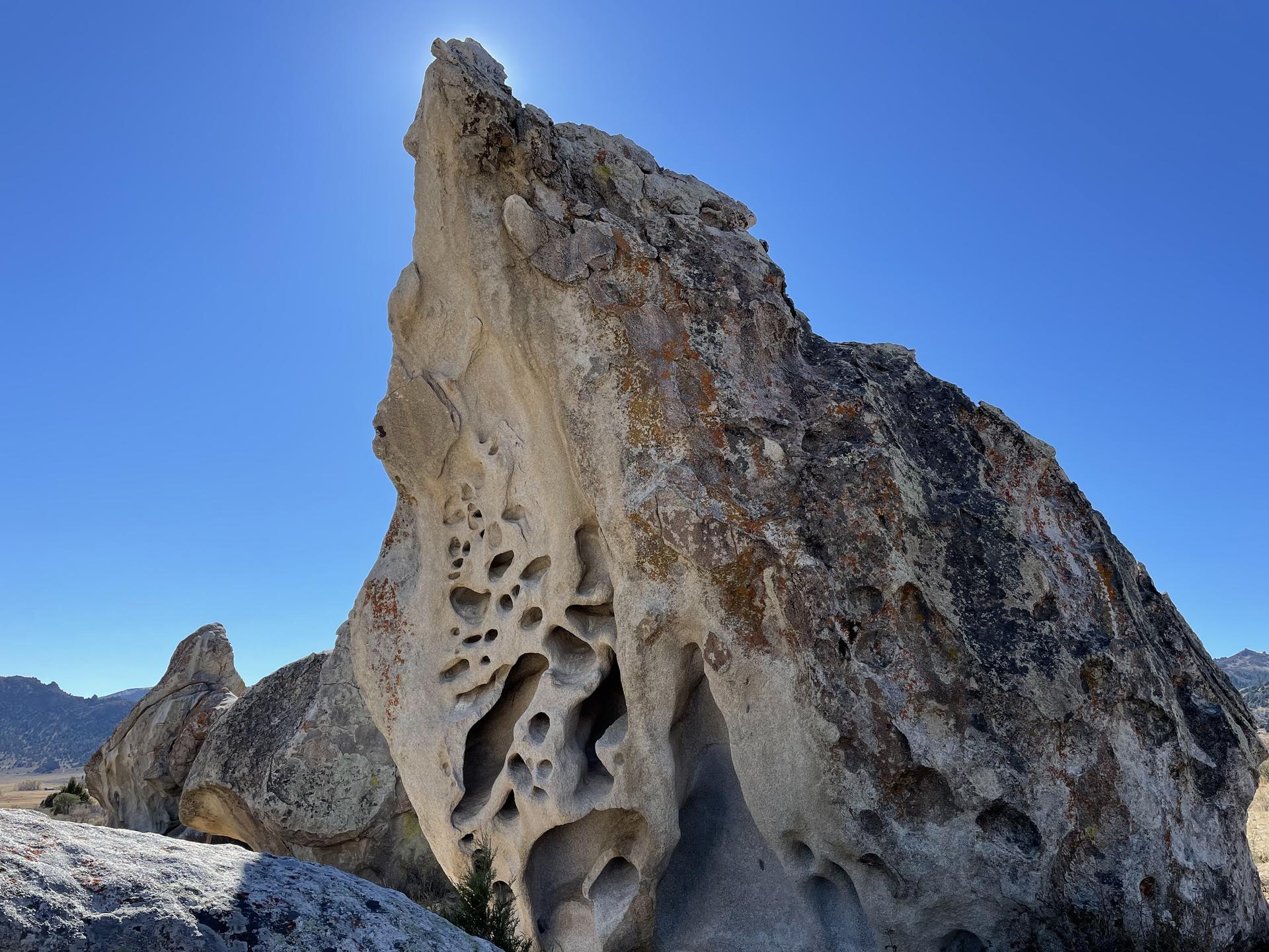 A large, eroded rock formation with many holes, backlit by bright sun.