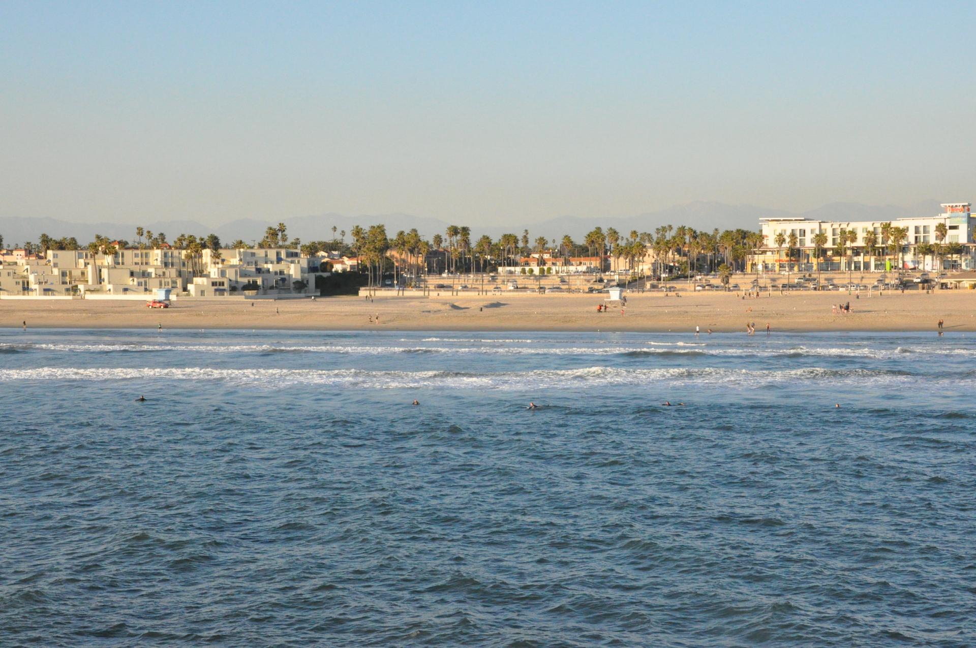 Wide view of the ocean, sandy beach, and distant buildings with palm trees.