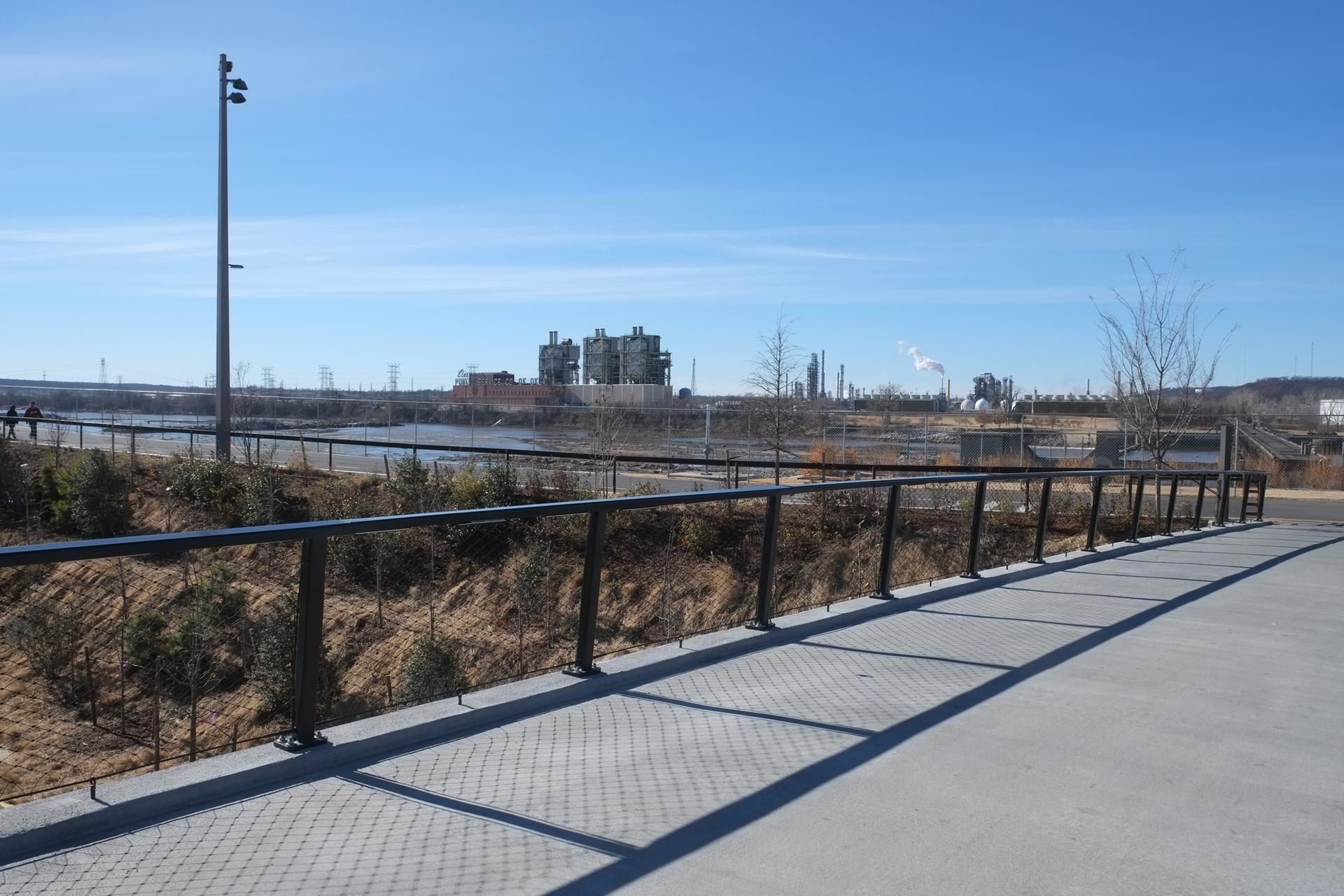 Concrete path with railing overlooking industrial buildings under a clear blue sky.