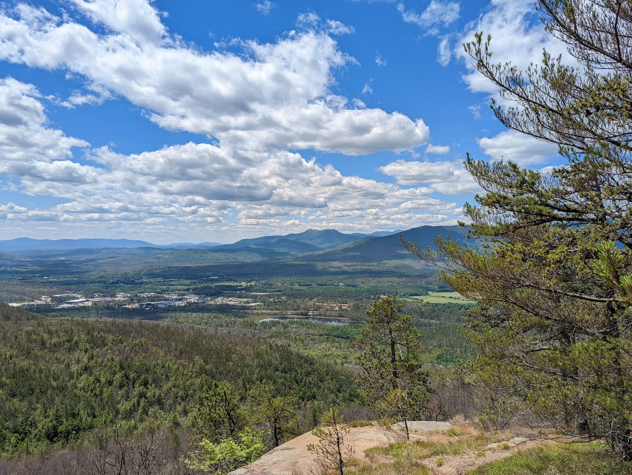 Panoramic view of a vast forested valley, distant mountains, and a town. - Peaked Mountain Trail