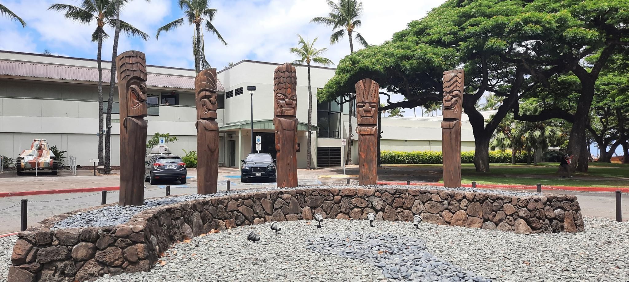 Five carved wooden statues in a stone planter with palm trees and buildings. - Honolulu to East Honolulu marathon loop