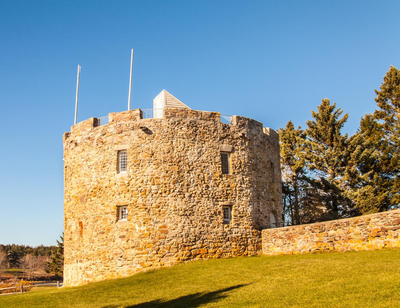 Ancient round stone tower on a sunny grassy hill with trees.