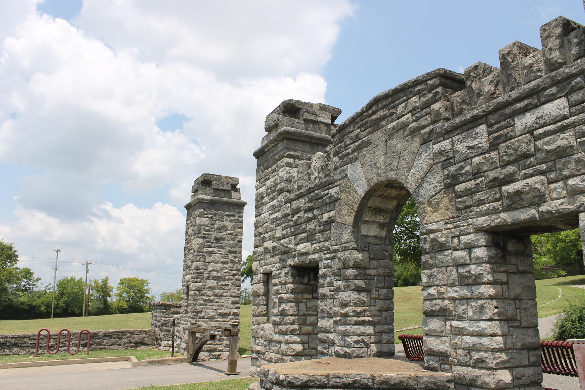 Large stone archway and pillars under a partly cloudy sky, with green grass.