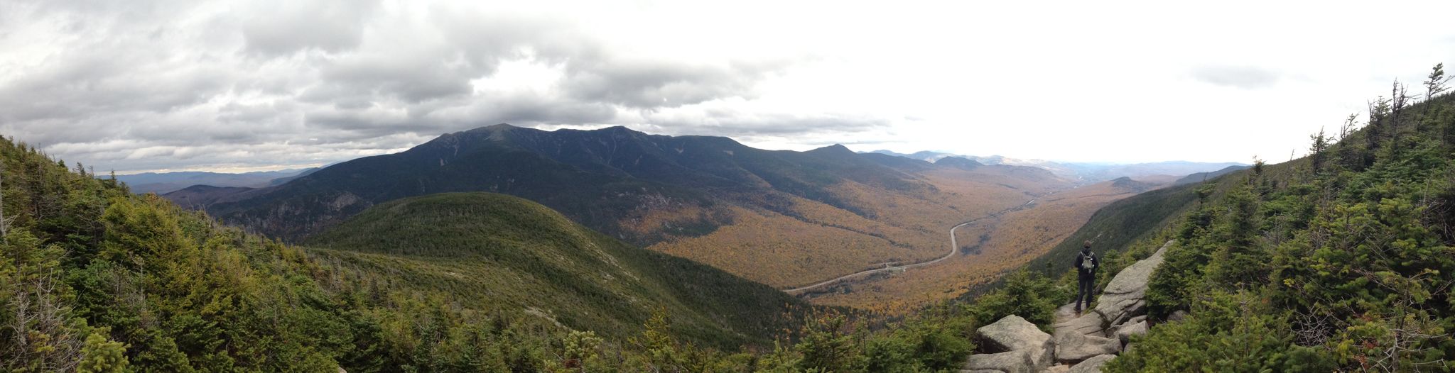Hiker on rocky outcrop overlooking a vast autumn mountain valley under cloudy skies. - Mount Martha via Cherry Mountain Trail — White Mountain National Forest