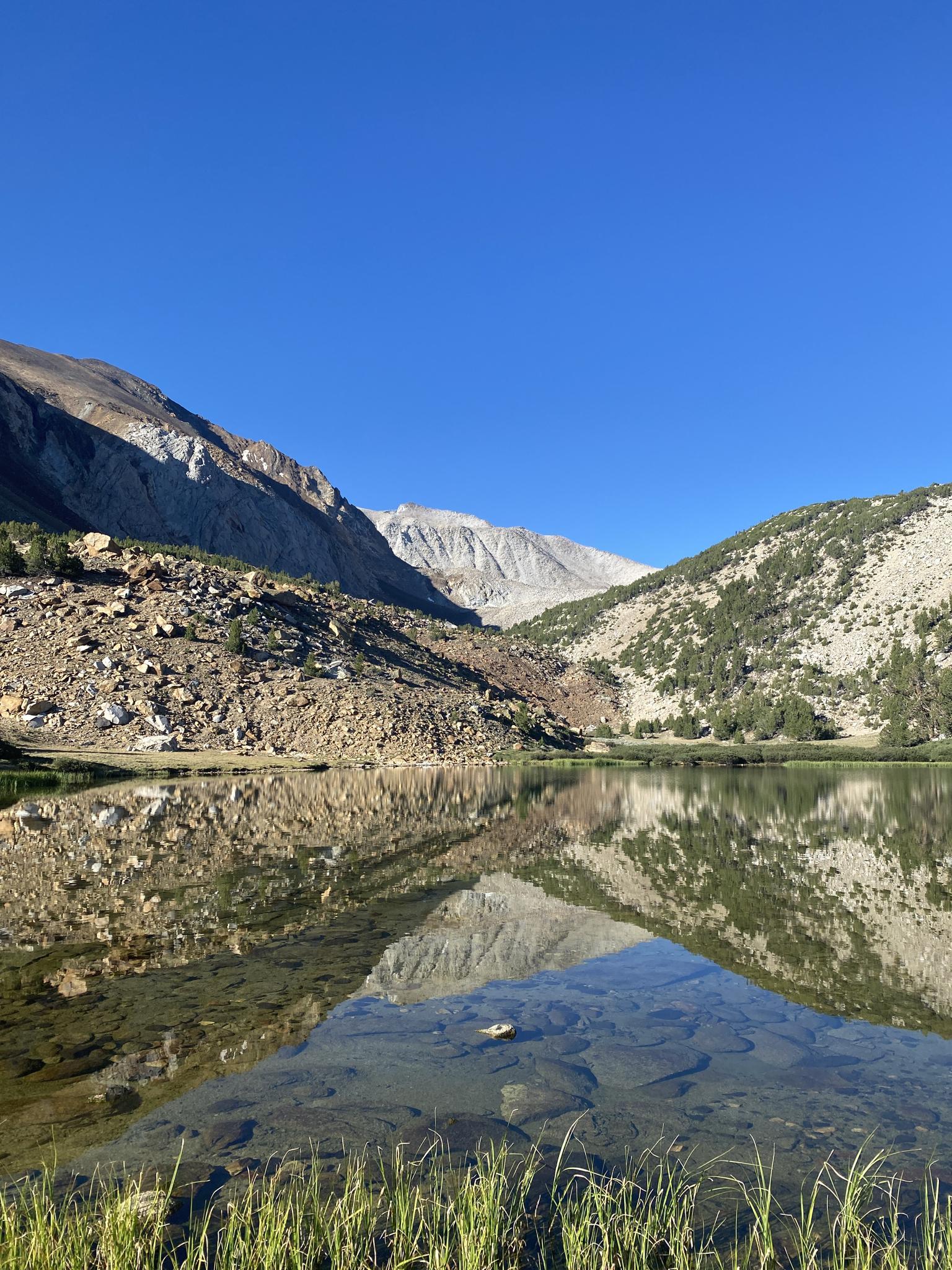 Clear mountain lake reflecting rocky slopes and blue sky on a sunny day.