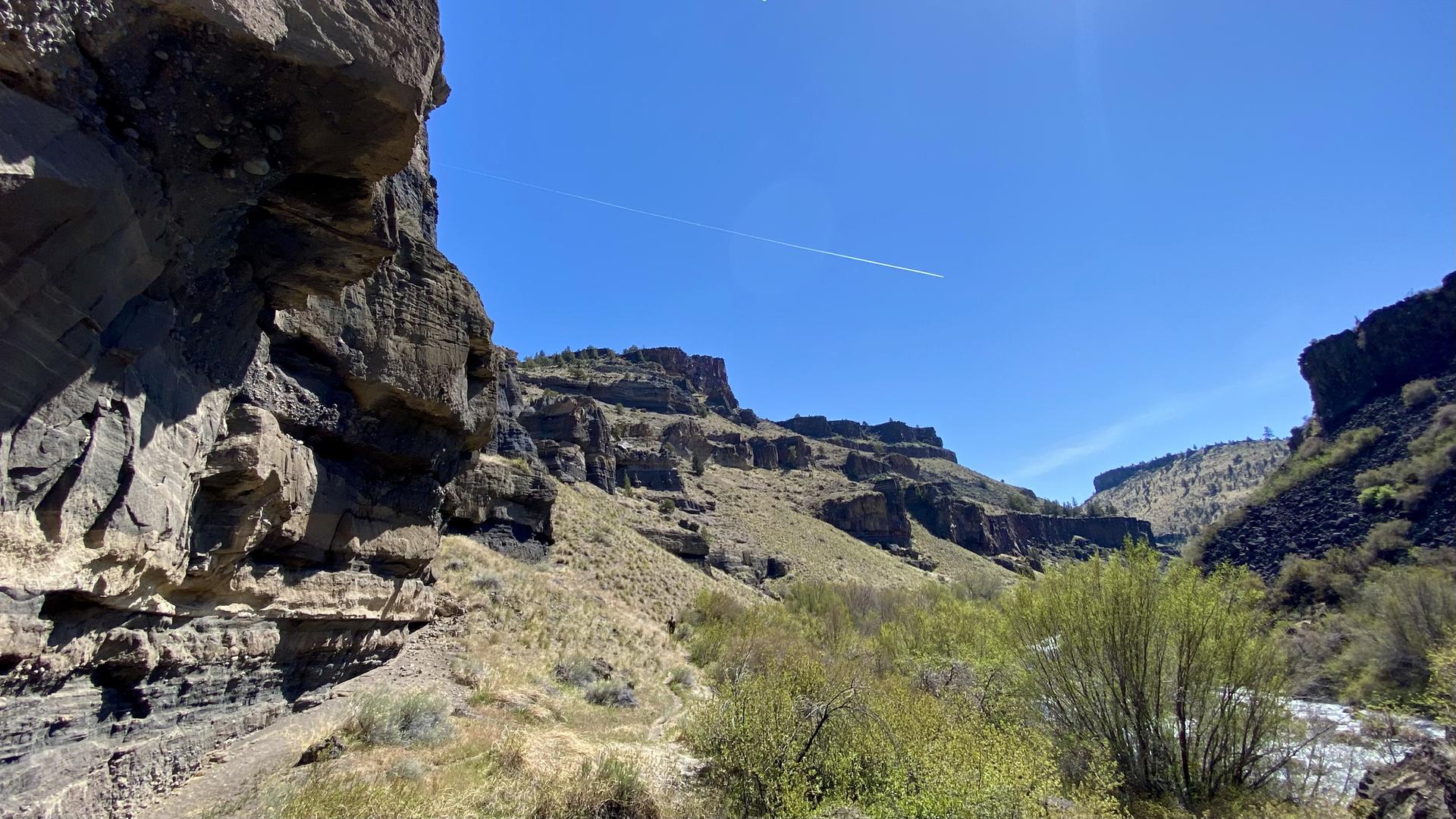 Rocky canyon walls and green shrubs under a bright blue sky.