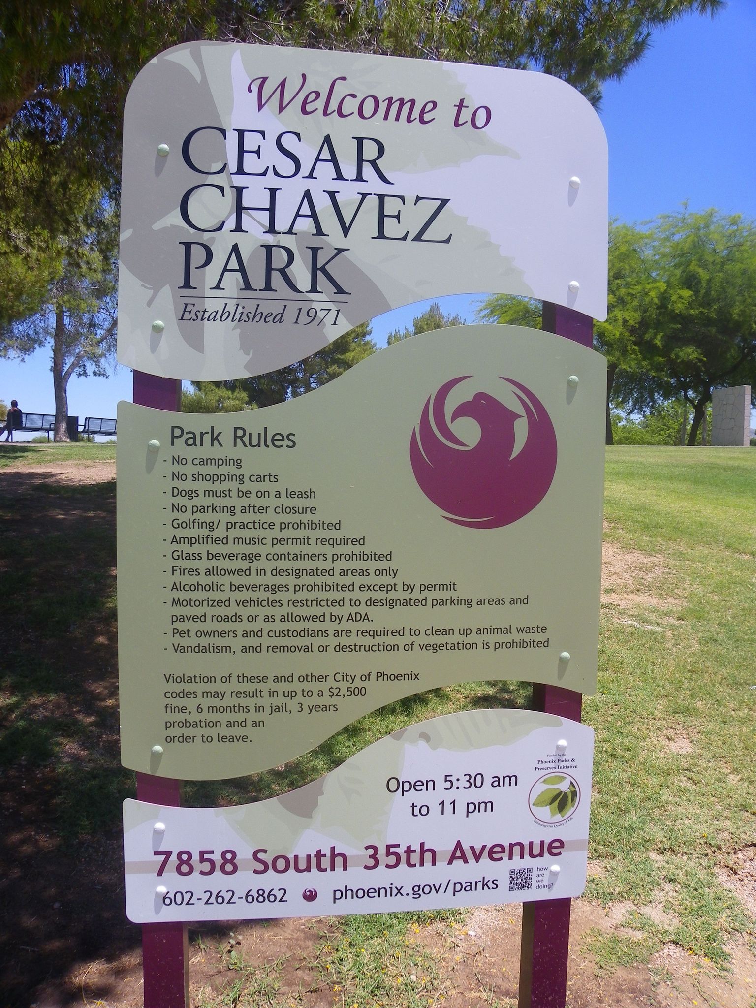 A park welcome sign with rules stands in bright daylight, a person walks in the background. - Cesar Chavez Park Walking Path