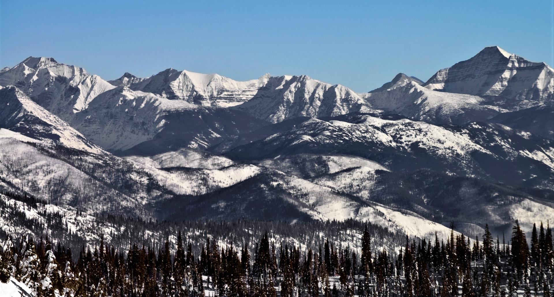 Majestic snow-covered mountain range under a clear, bright blue sky.