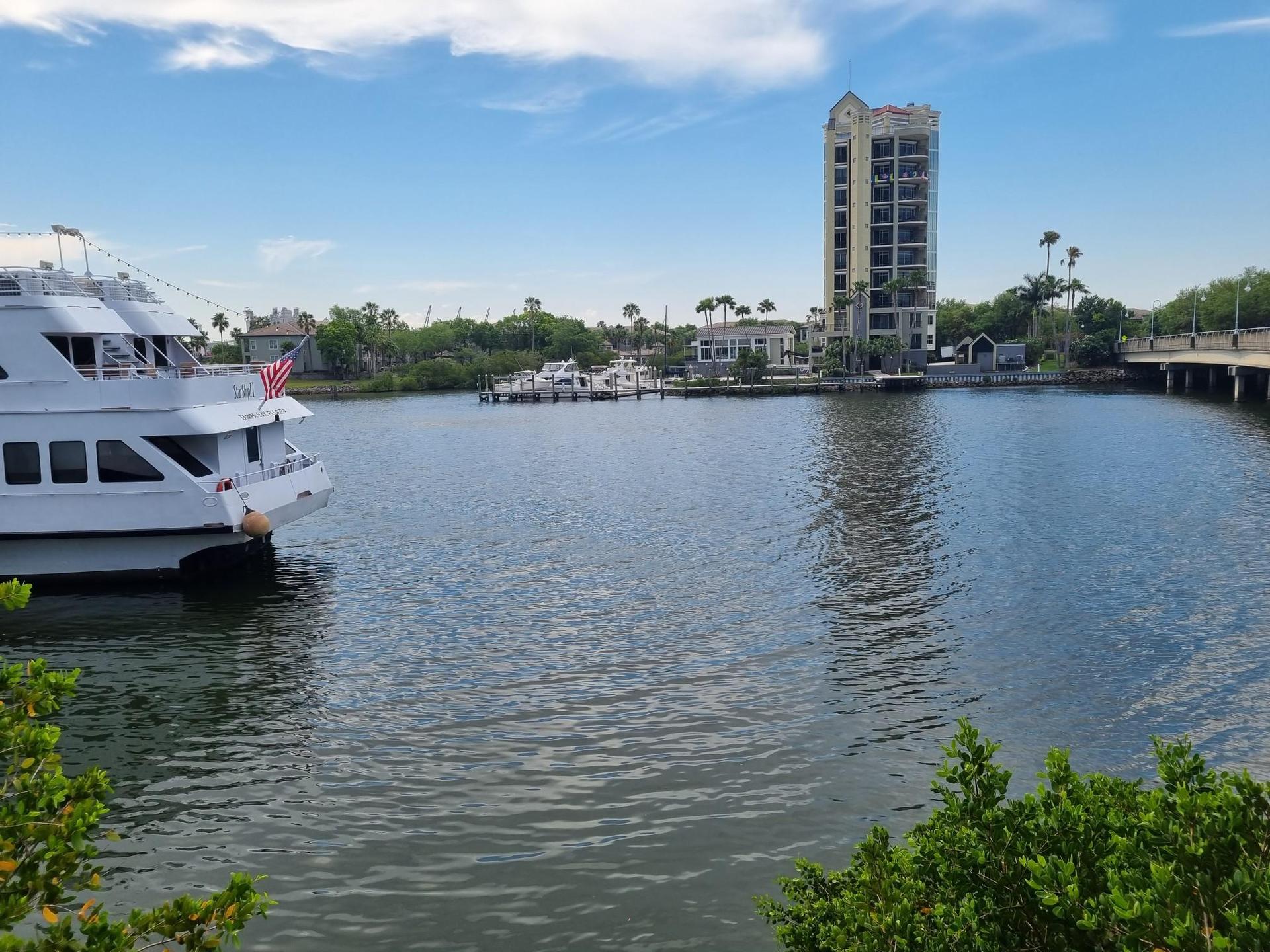 Large white boat docked on a river with a tall building nearby.