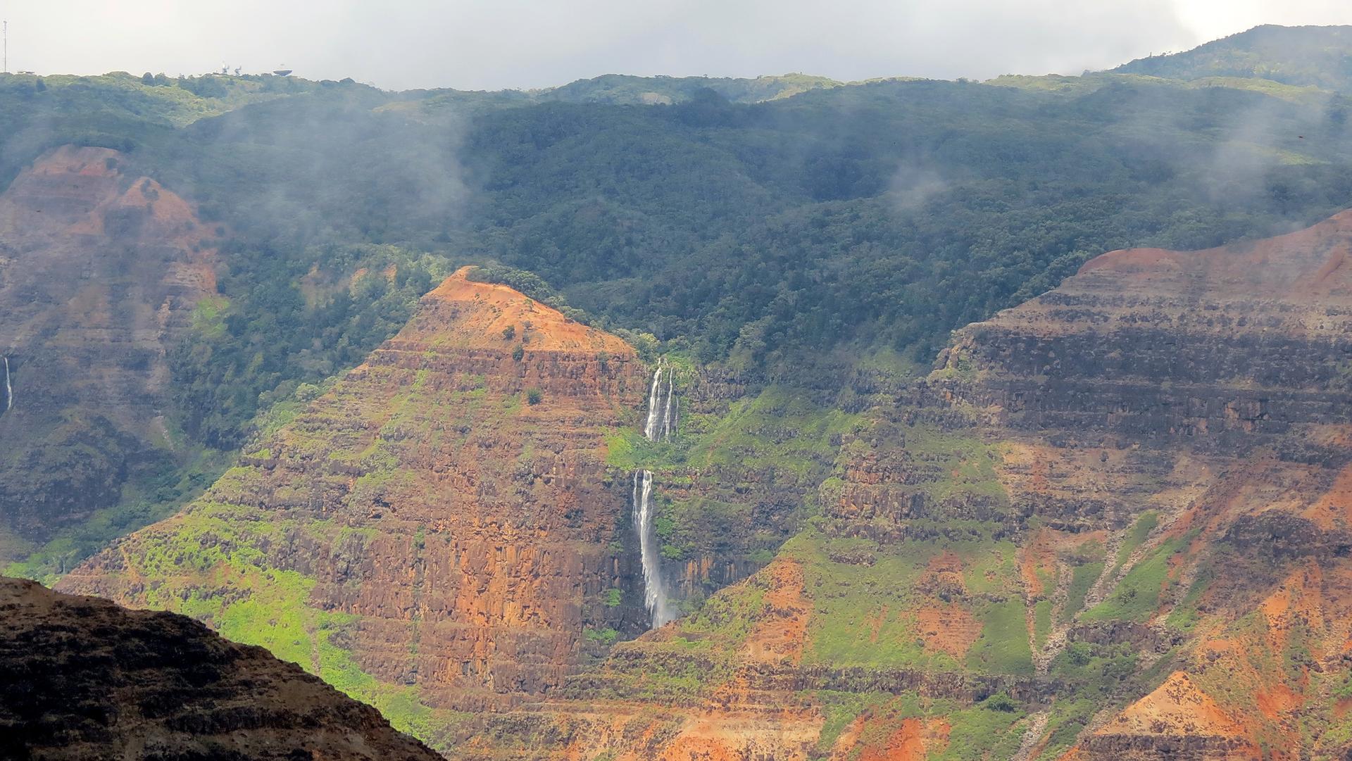 Waterfall cascades down a misty, green and brown canyon landscape.