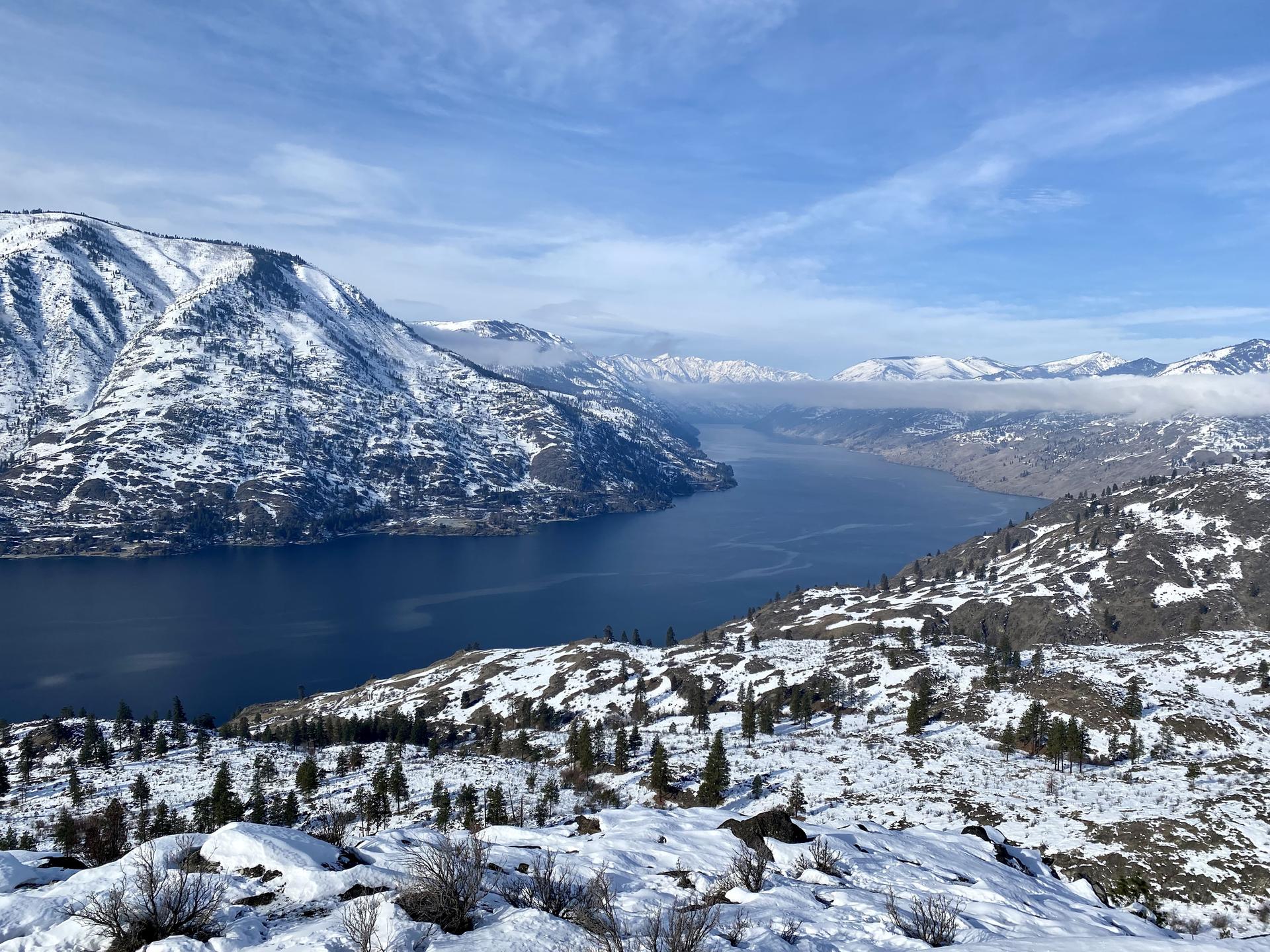 Vast river winding through snow-covered mountains under a bright, cloudy sky.