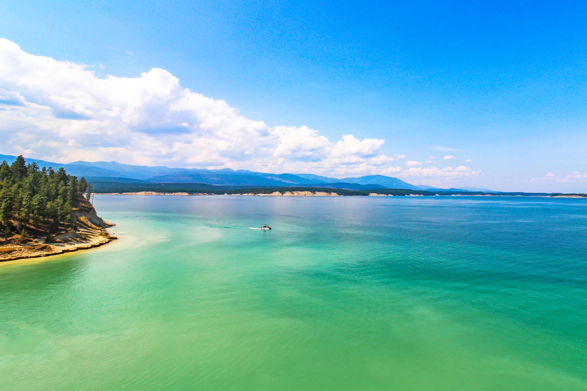 Bright sunny day over turquoise water with a boat and forested shoreline.