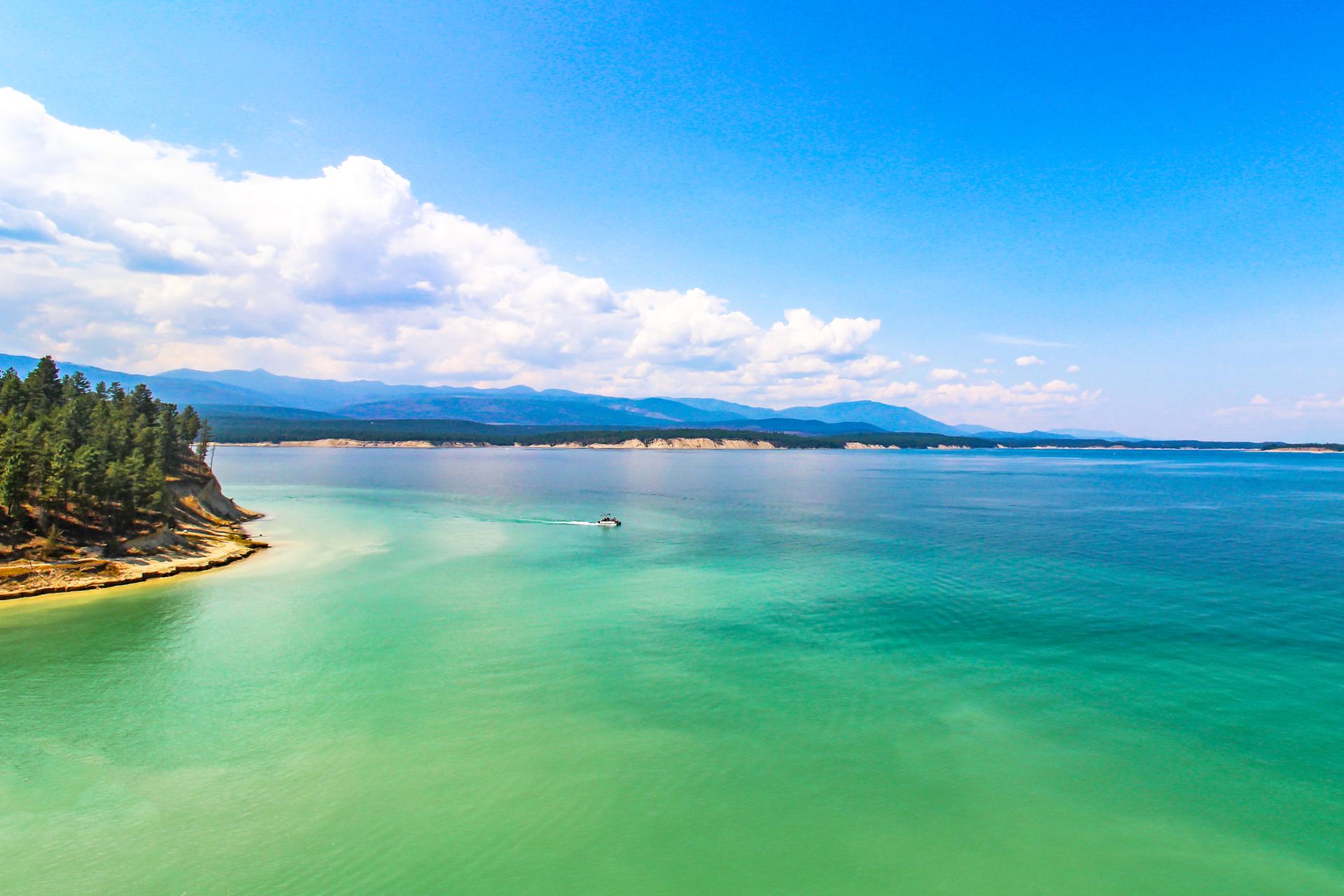 Bright sunny day over turquoise water with a boat and forested shoreline.