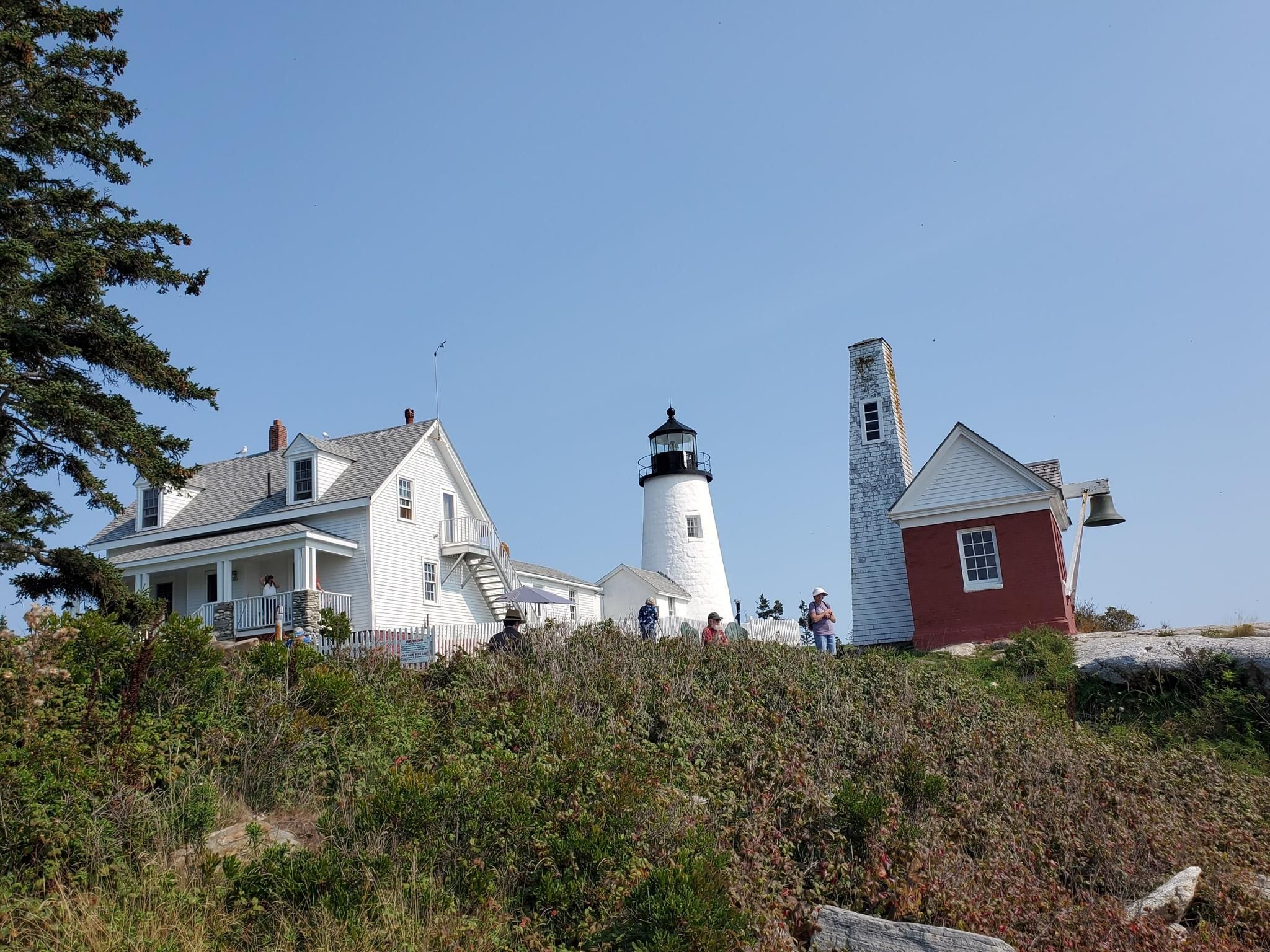 White lighthouse, red bell tower, and house on a sunny hill with people. - Twin Villages to Pemaquid Lighthouse & Fort William Henry loop