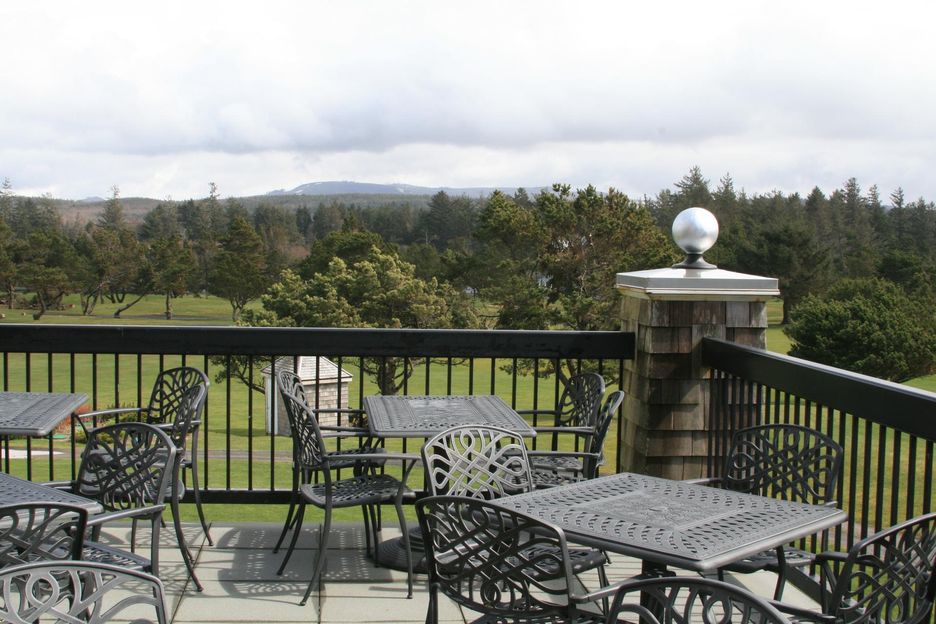 Outdoor patio with metal tables and chairs overlooking a golf course on a cloudy day.