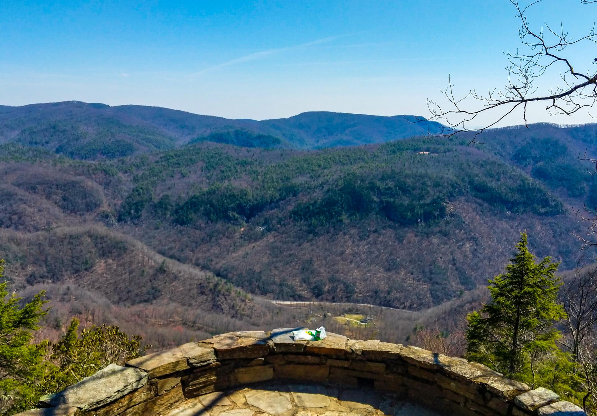 Sunny mountain vista from a stone overlook, with distant forested hills.