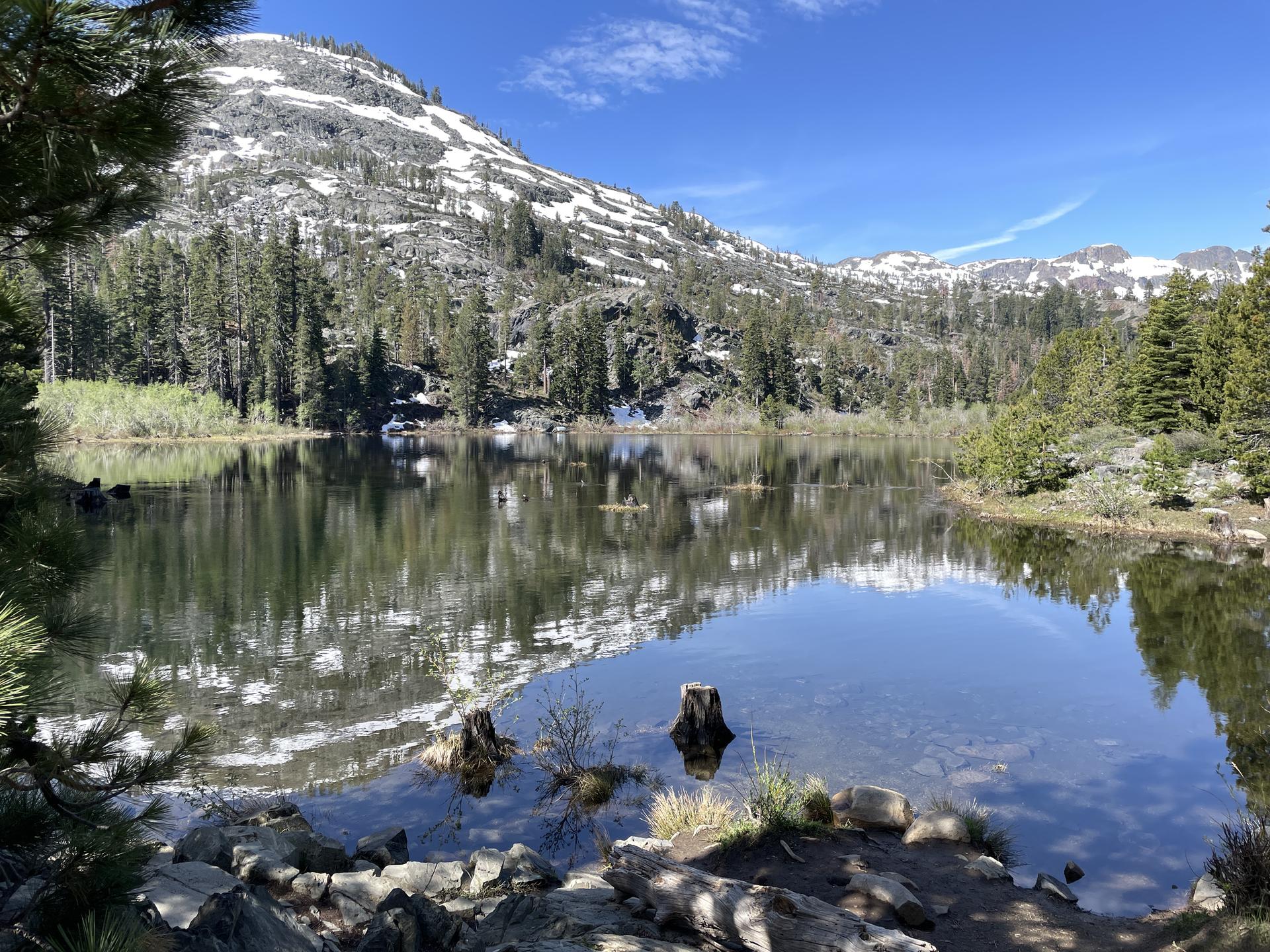 A still lake reflects snow-dusted mountains and green pine trees.