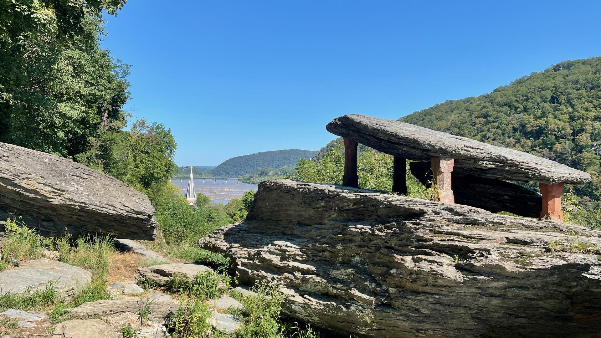 Large rock formations overlook a river and distant hills on a sunny day.