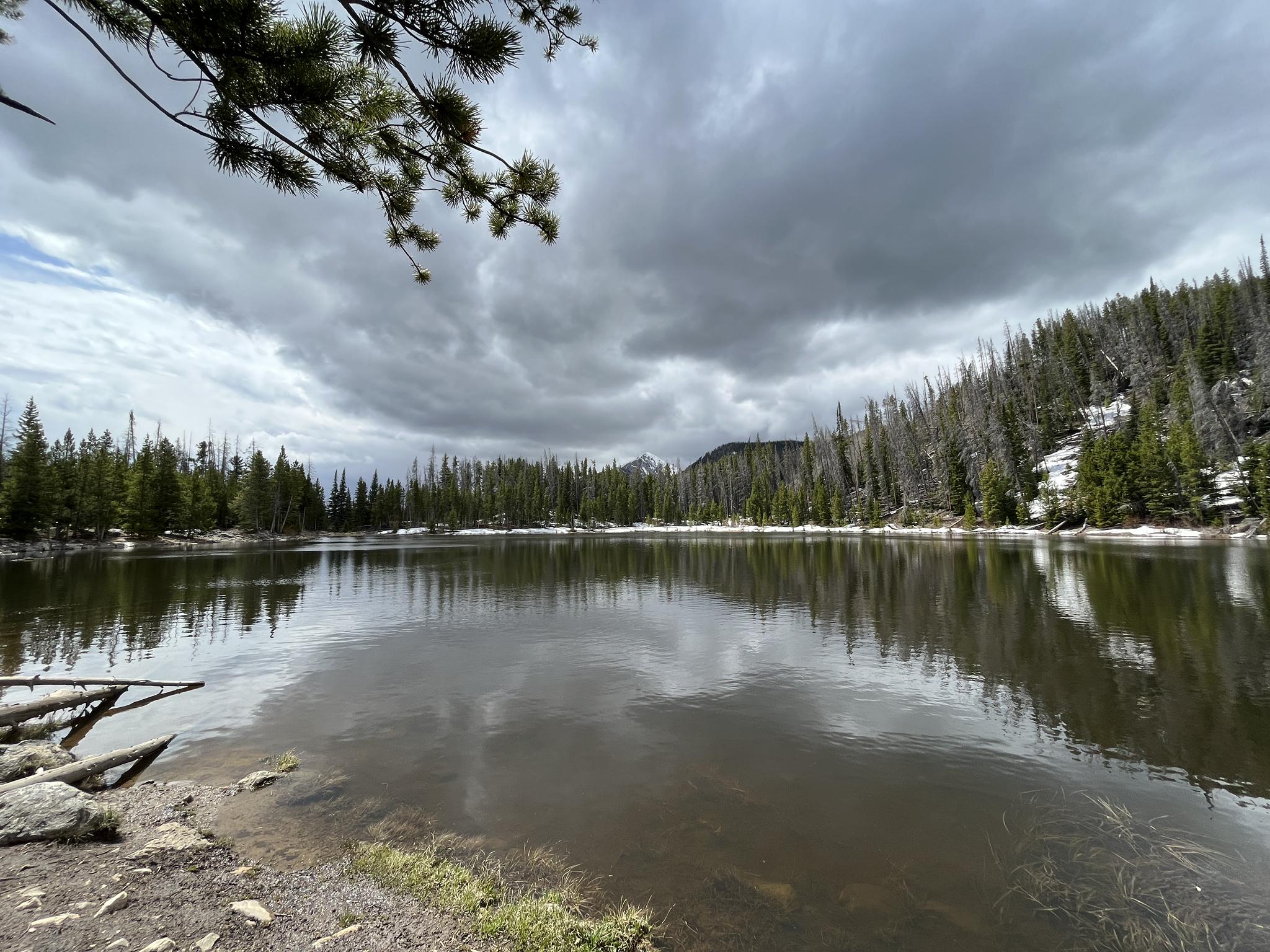 A wide lake reflecting a dark, cloudy sky and distant forested mountains.