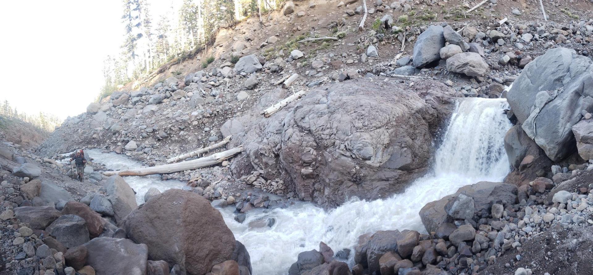 A rushing river flows over rocks, forming a small waterfall.