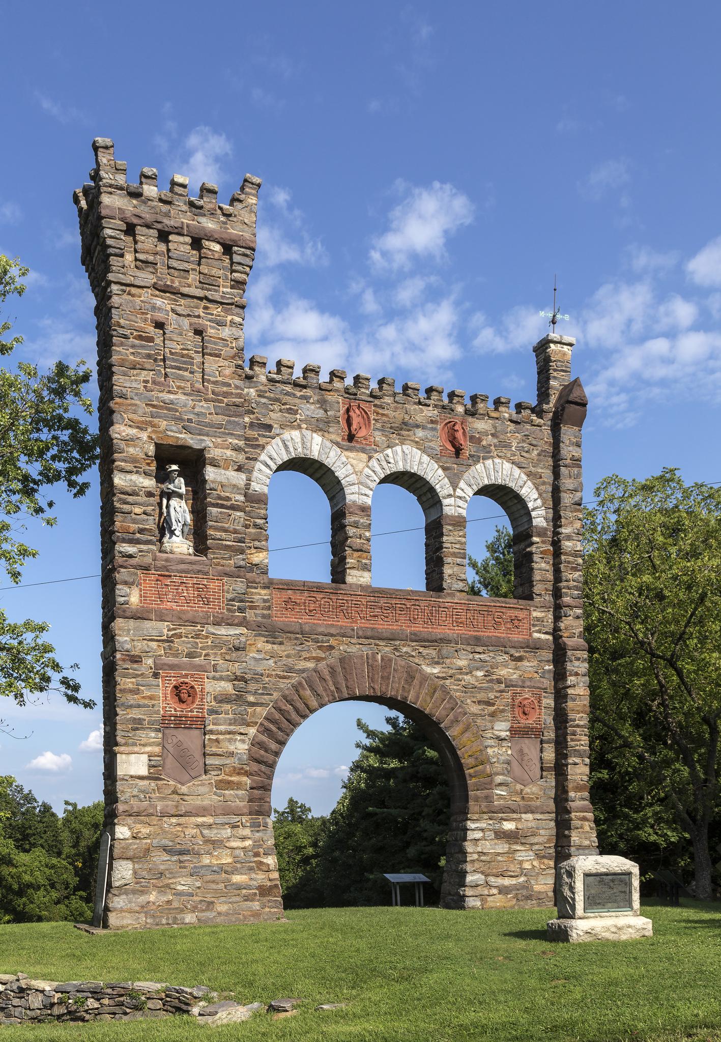 Large stone archway with castle-like features on a grassy lawn.
