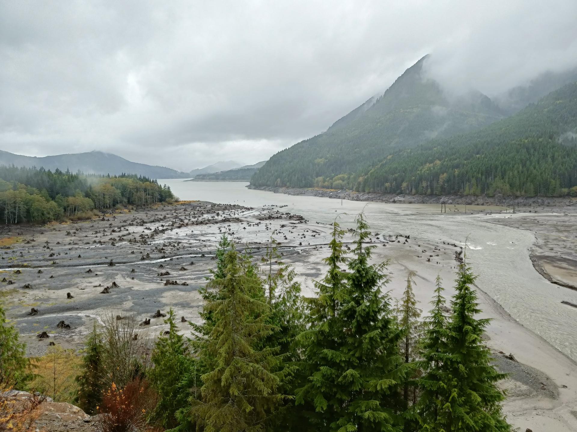 Overcast mountain landscape with a wide, exposed riverbed and narrow river.