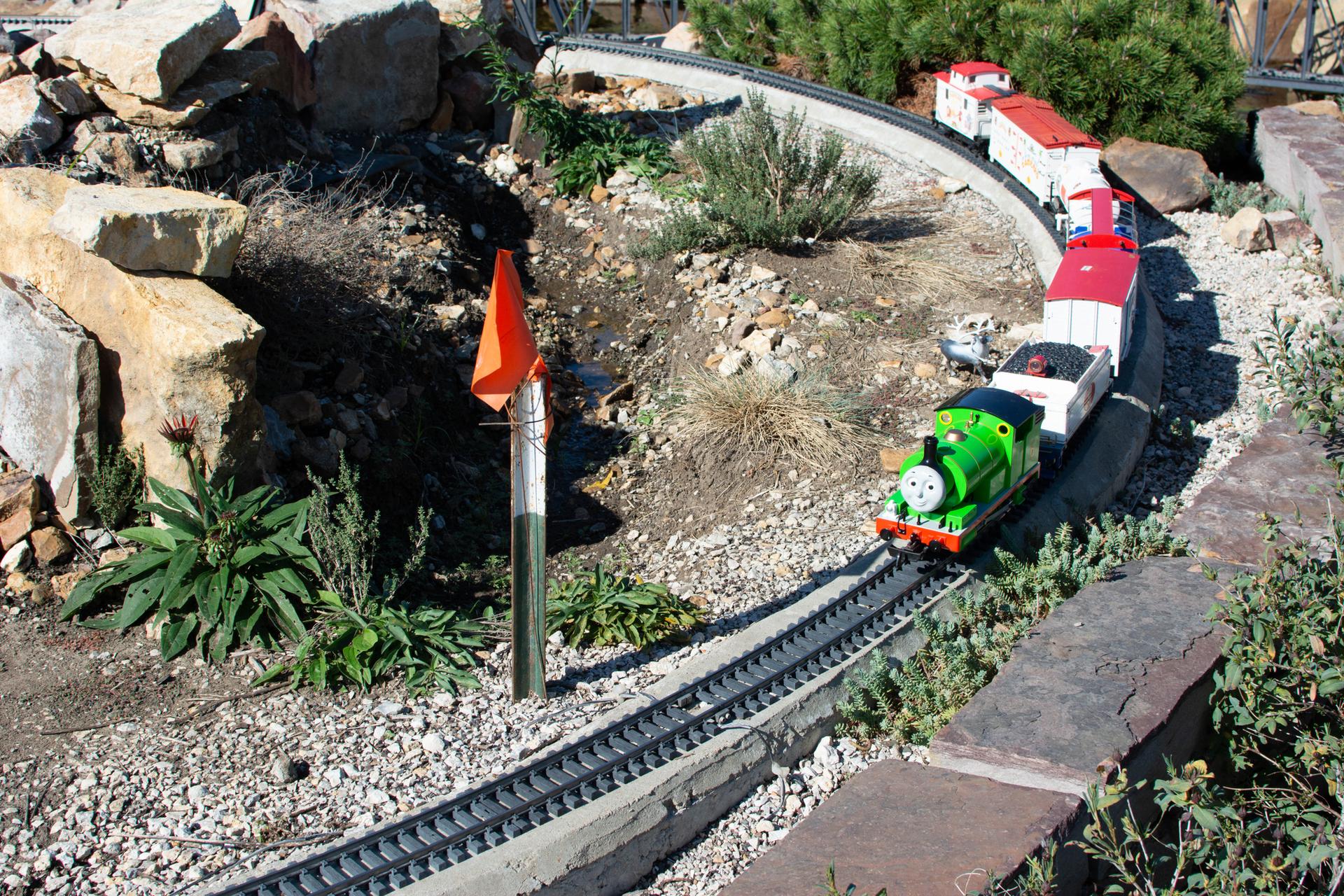 A green model train on tracks winds through a rocky outdoor garden.