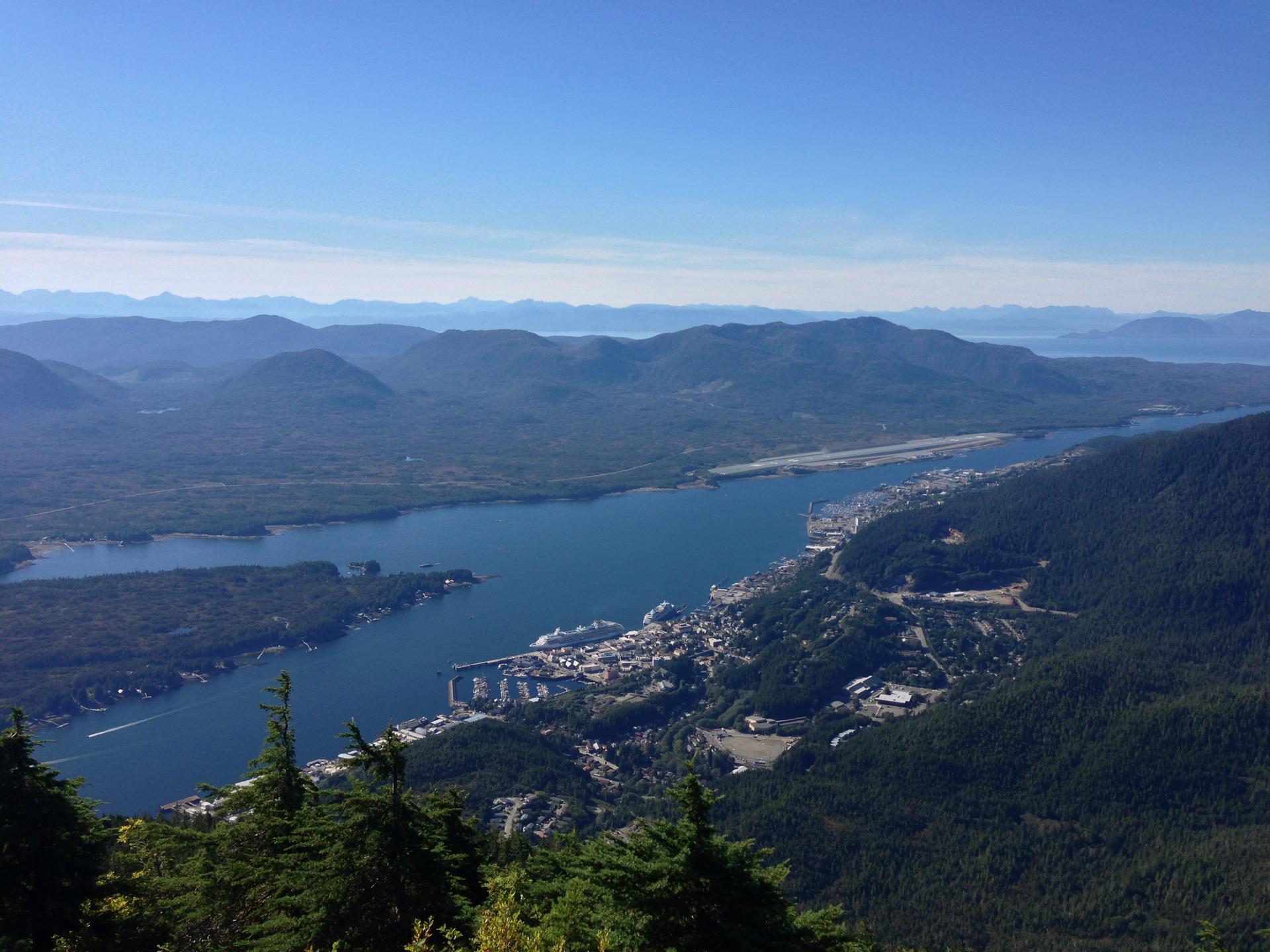 Wide aerial view of a town, harbor, and airport by a river, clear sky.