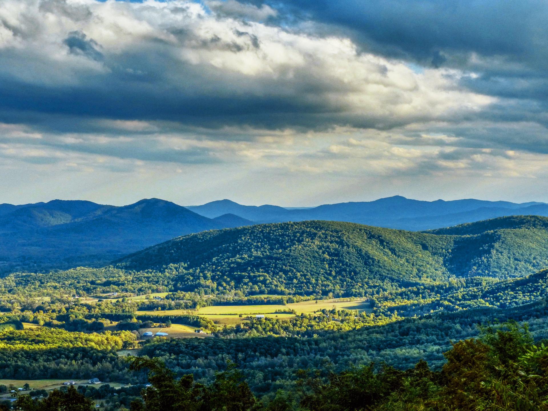 Green rolling mountains and valleys under a dramatic cloudy sky.